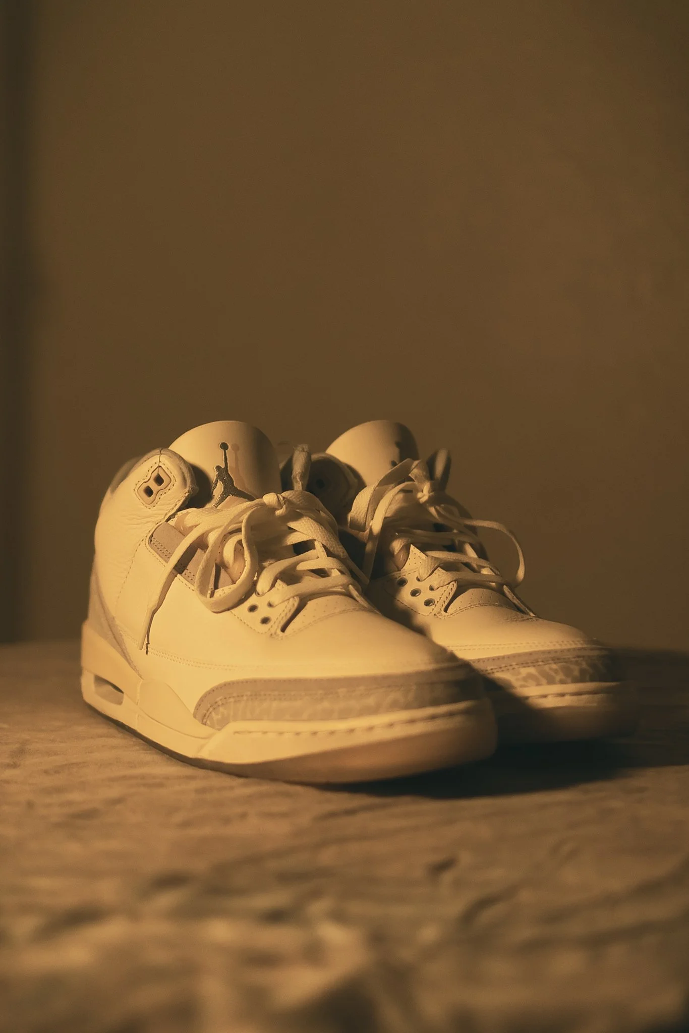 Pair of white sneakers with gray accents and laces, displayed on a surface in soft lighting.