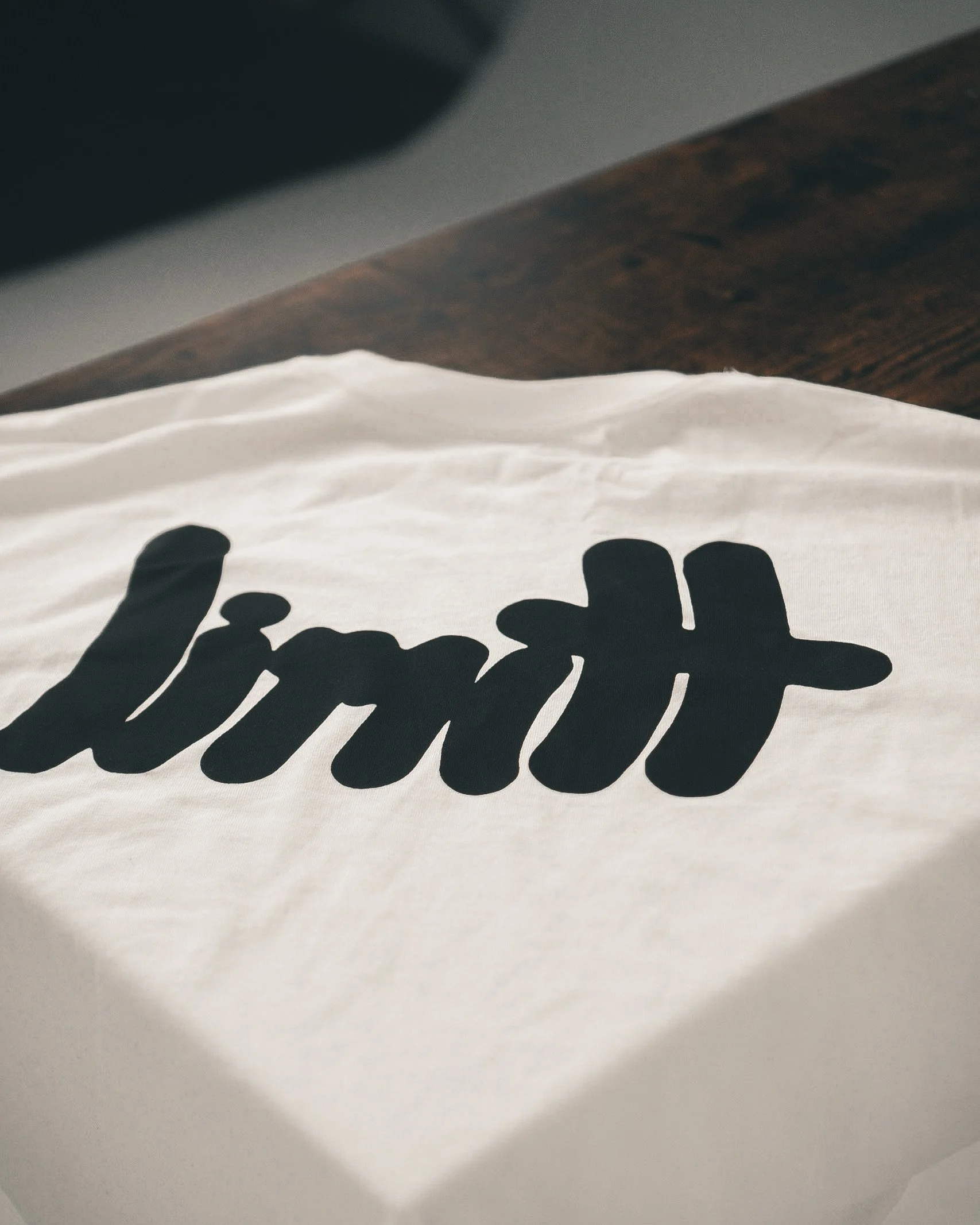 White t-shirt with 'limit' printed in black italic script on a table