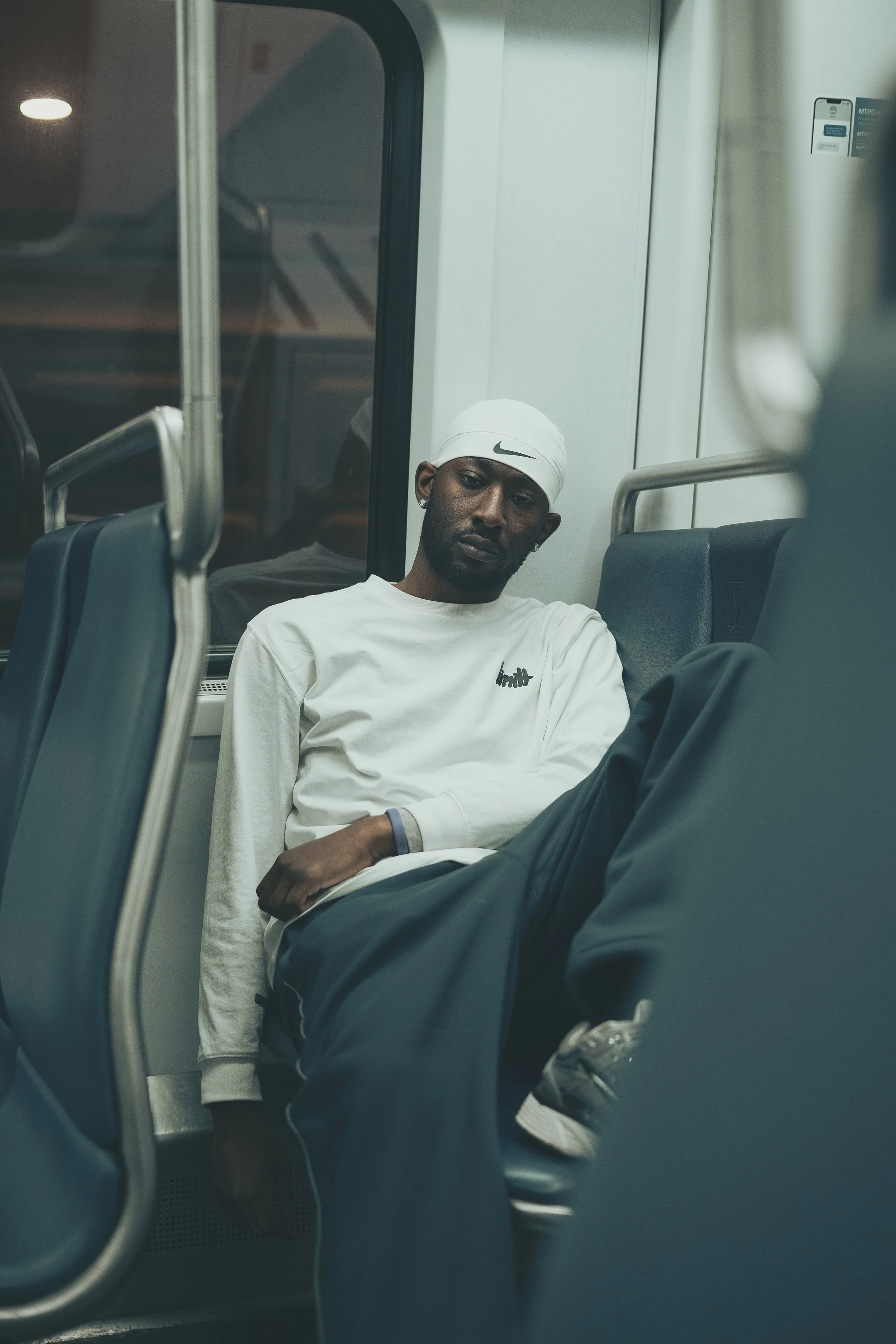 Man in white shirt and headband sitting on a train seat.