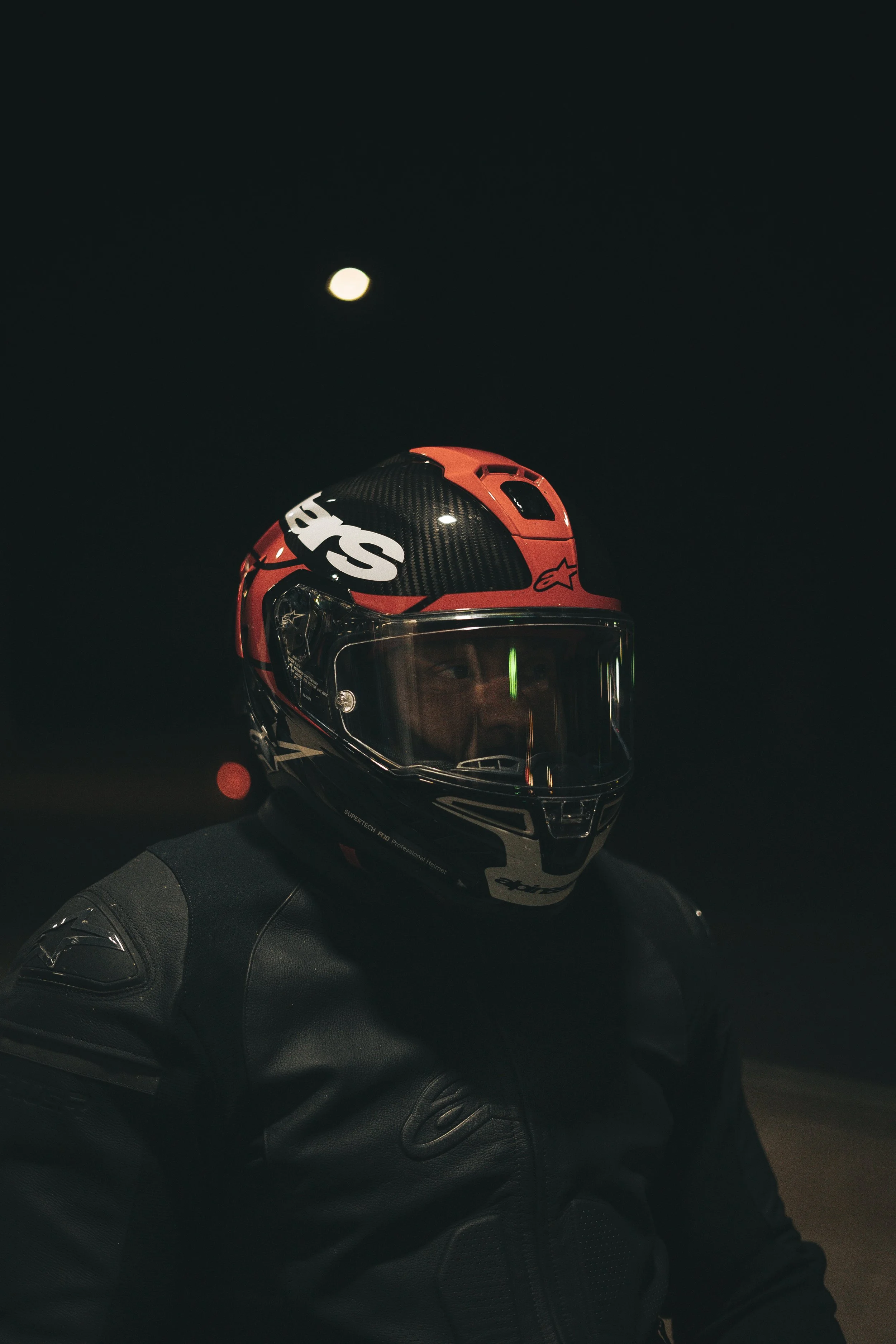 Person wearing a black and red motorcycle helmet and black jacket at night