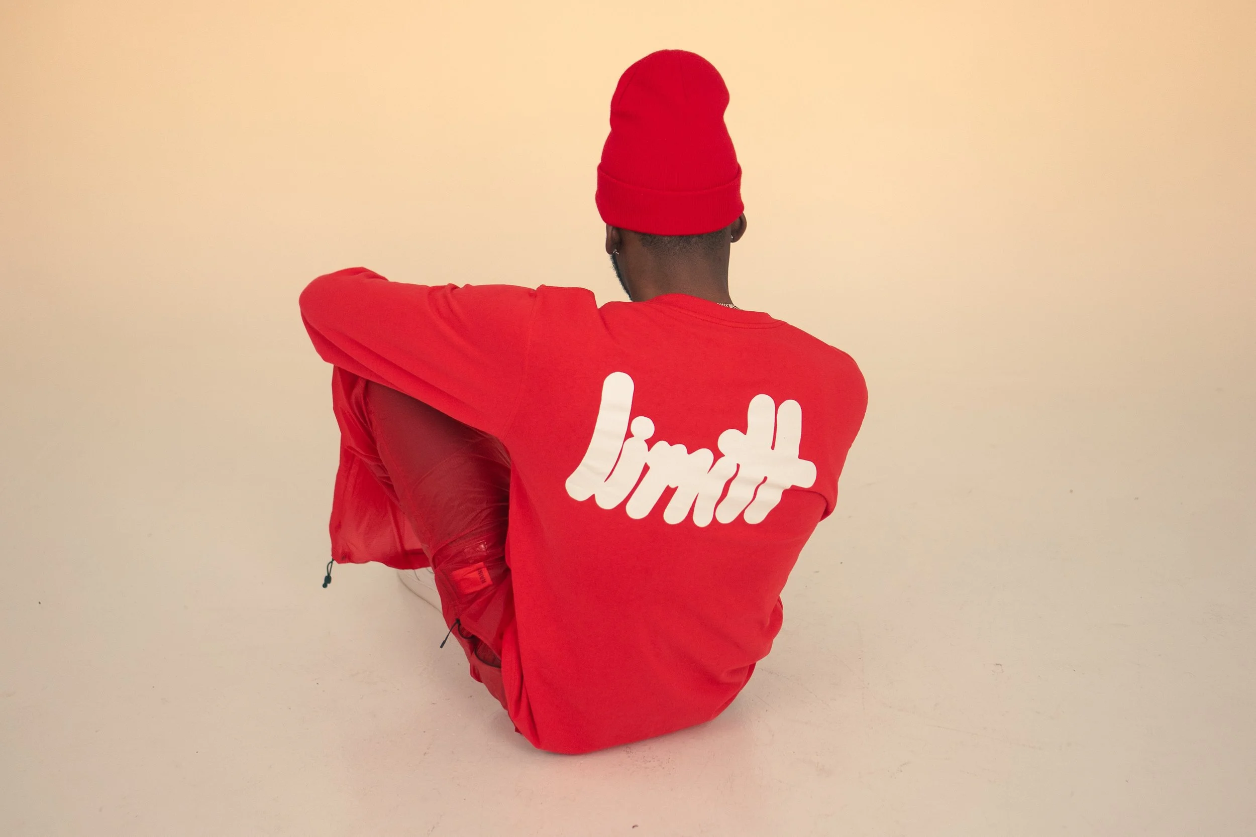 Person in red beanie and red sweatshirt with "limit" text on back, sitting on floor.