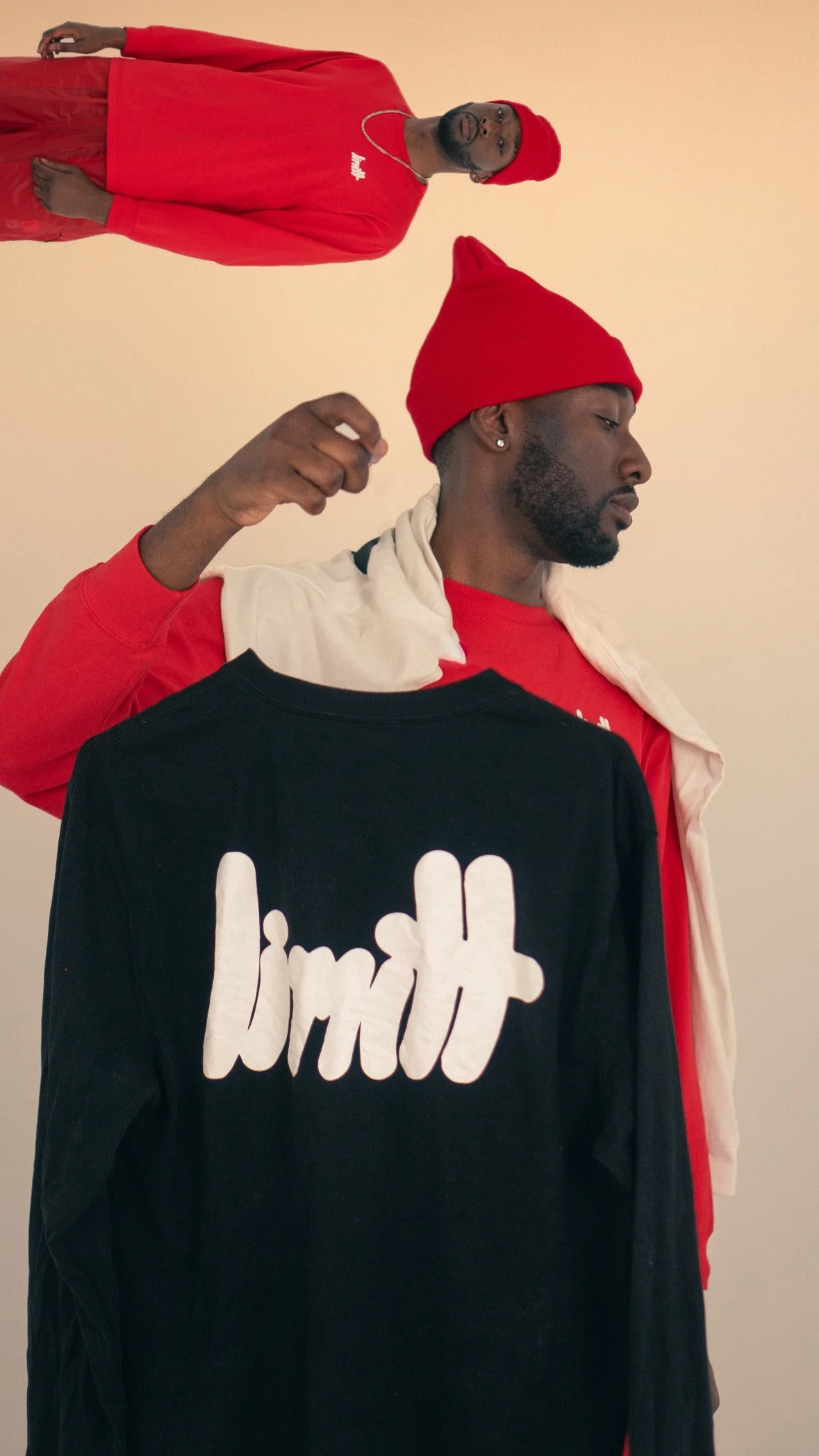 Man wearing a red beanie and red shirt, holding a black shirt with "limit" written on it, against a neutral background.