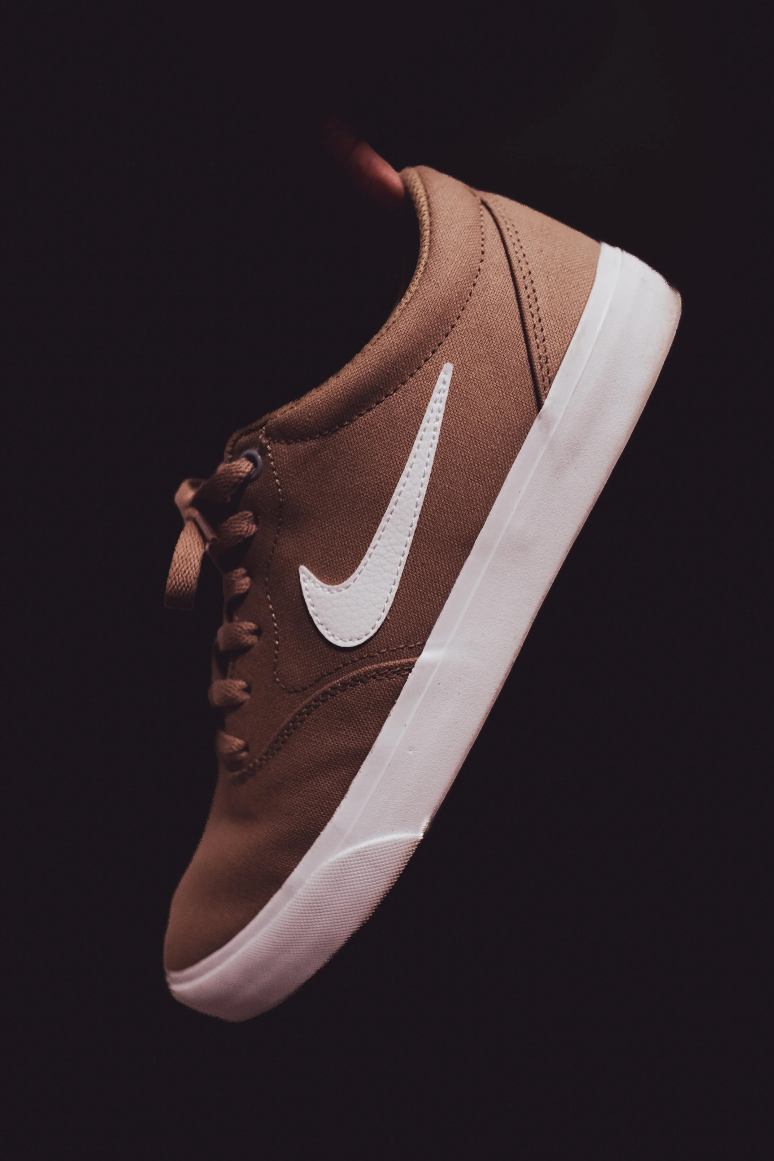 Brown sneaker with white swoosh logo on black background