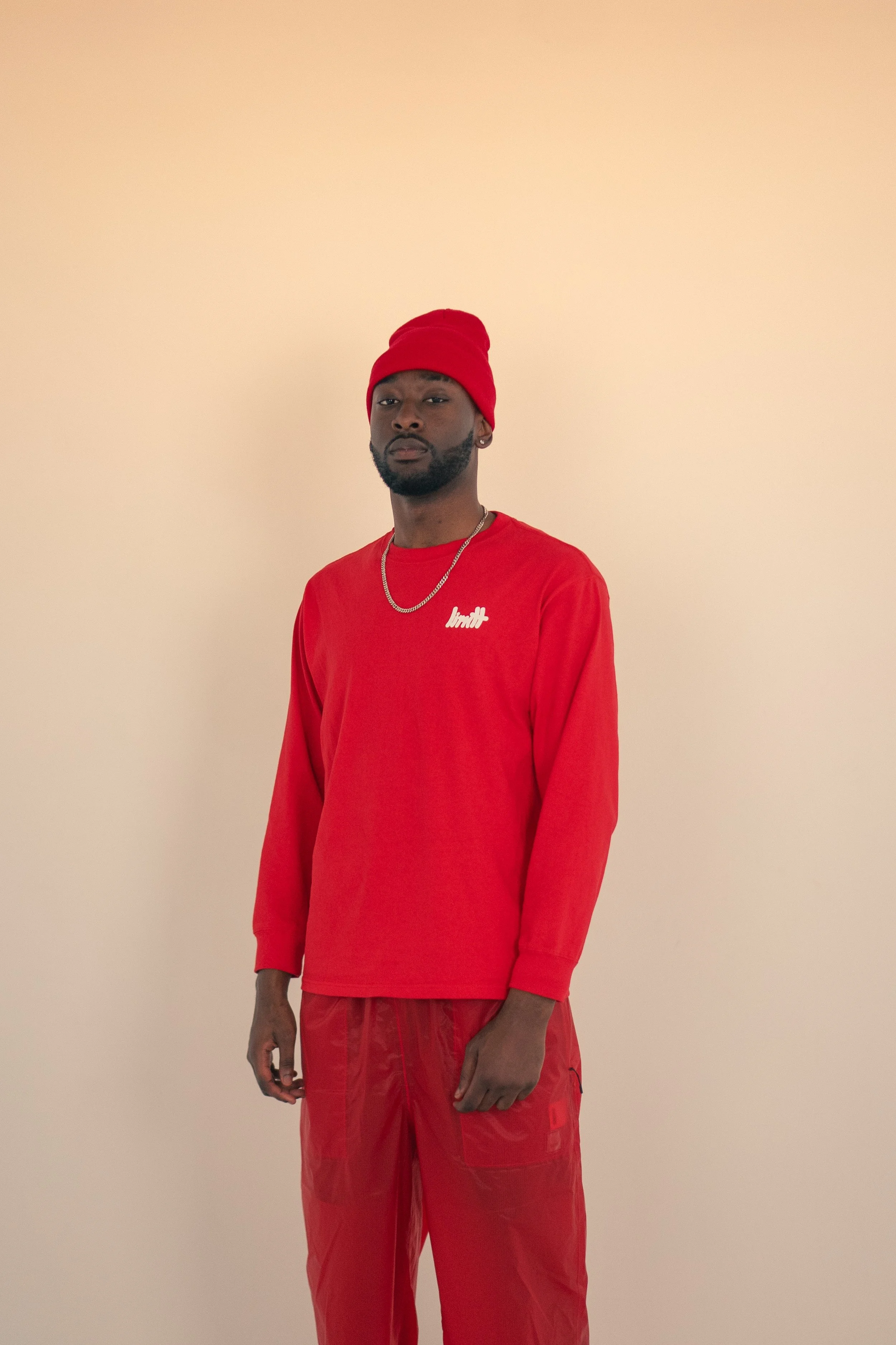Man wearing red beanie, red long-sleeve shirt, and red pants, standing against a beige background.