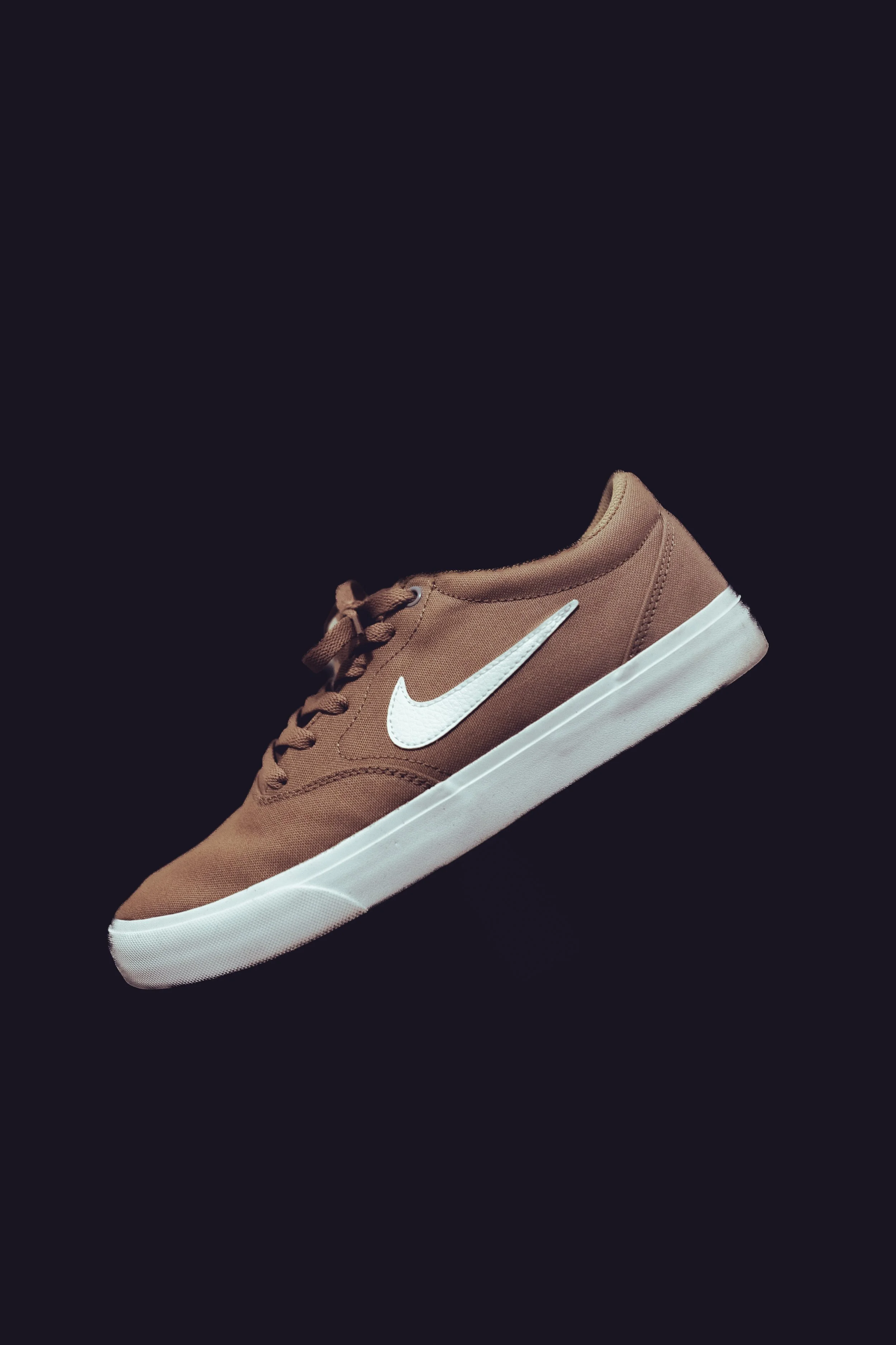 Brown sneaker with white swoosh logo and sole on dark background.