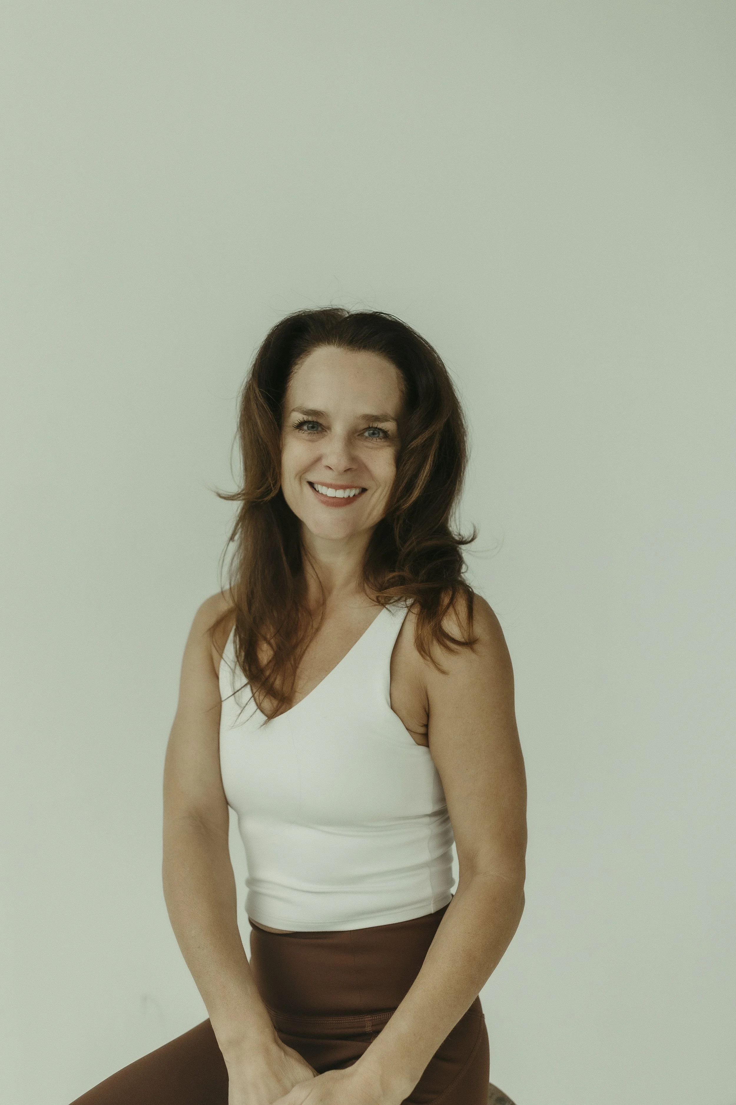 A woman with shoulder-length brown hair smiling, wearing a sleeveless turquoise top, against a black background.