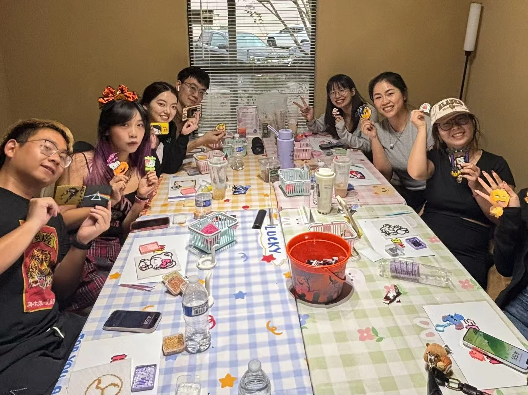 A group of ten people sitting around a decorated table with drinks, snacks, and stickers, smiling and posing for the camera in a casual indoor setting.