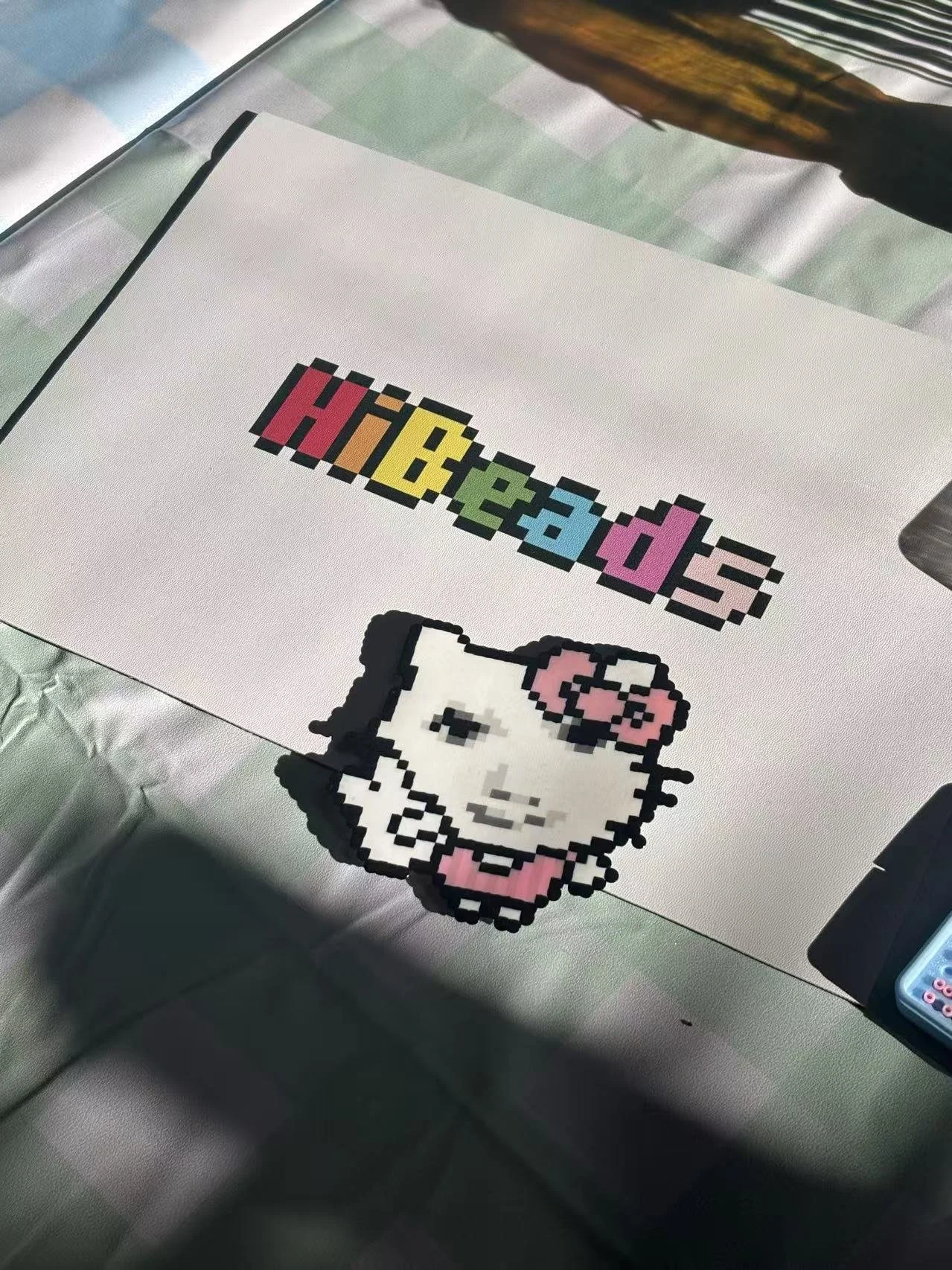 Pixel art of Hello Kitty with pink bow and collar, alongside colorful text spelling "HiBeads" on a white background.