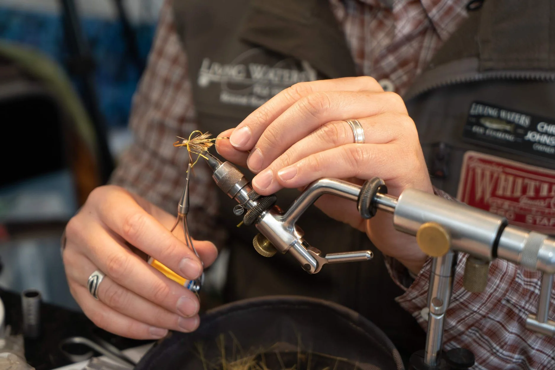 Person using fly tying tool to craft a fishing fly with feathers and thread.