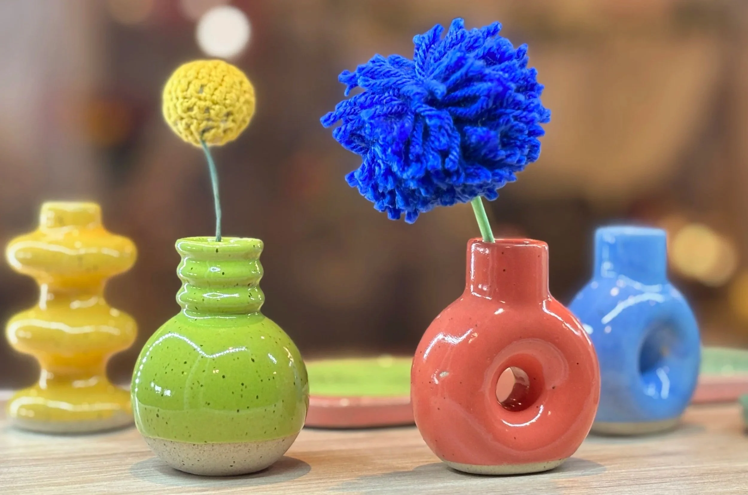 Colorful ceramic vases with yarn flowers on a wooden surface.