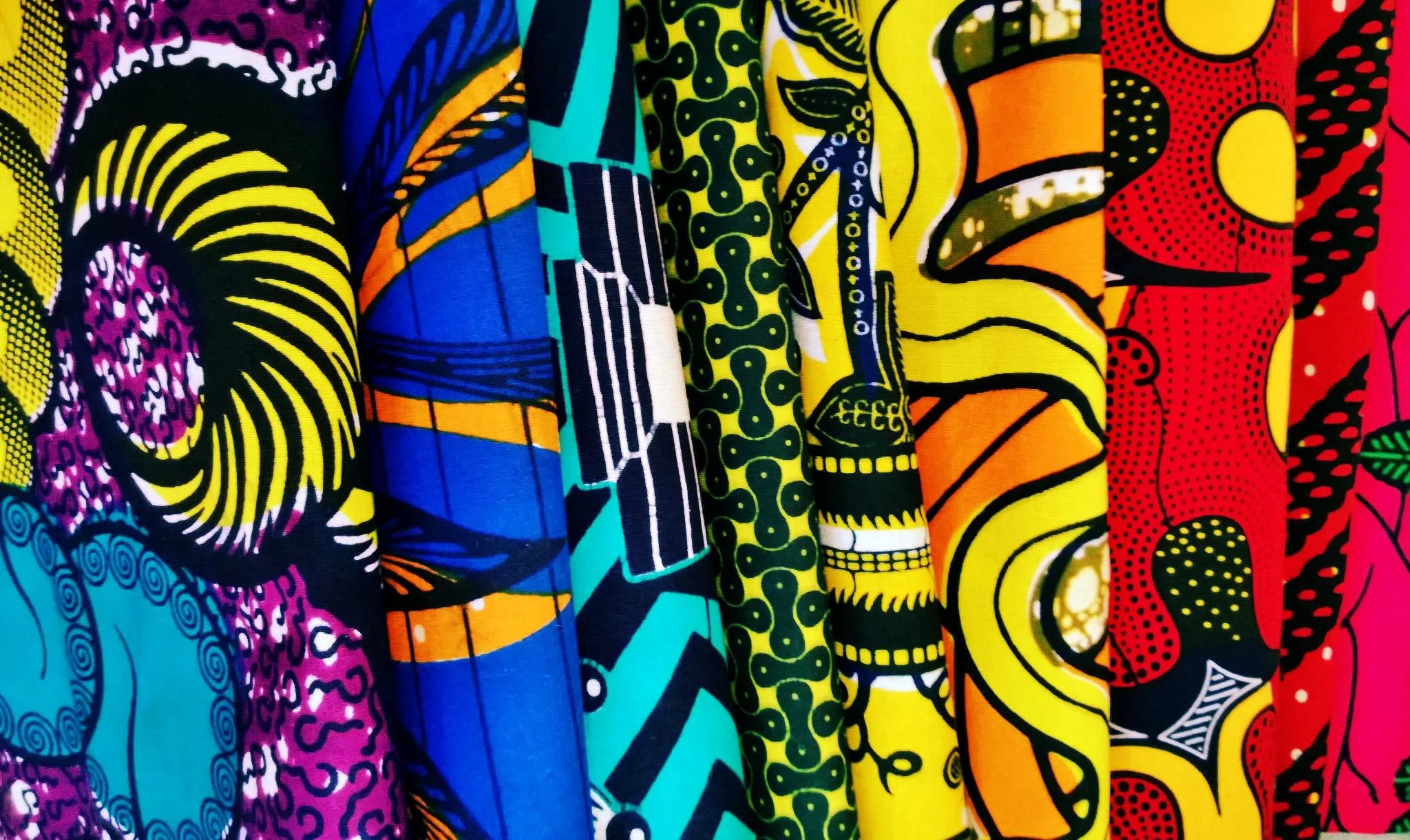 Close-up of colorful fabric with vibrant African-inspired patterns in purple, yellow, blue, green, orange, red, and pink.