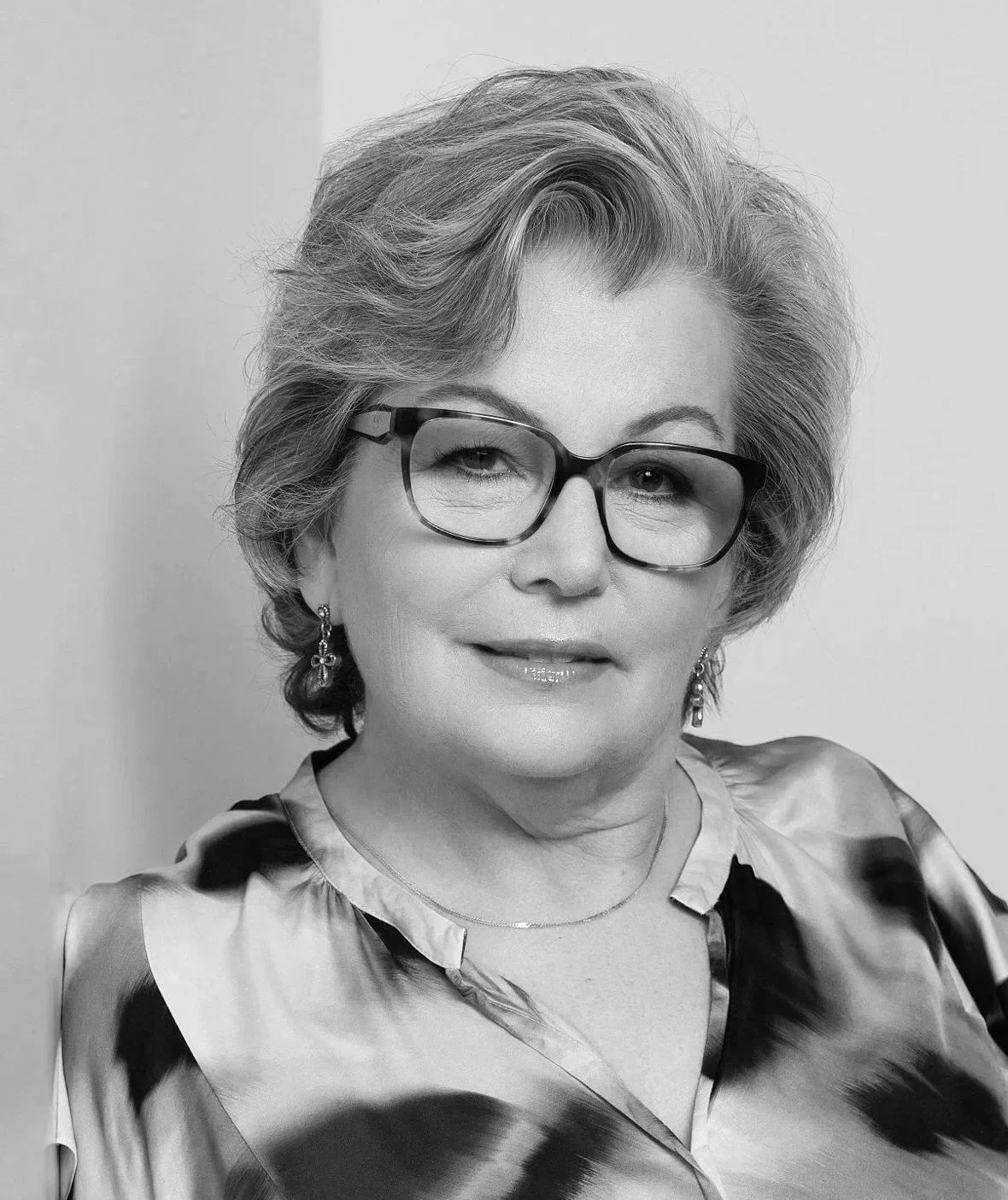 Black and white portrait of Carrie Gataiant wearing glasses, earrings, and a patterned blouse.