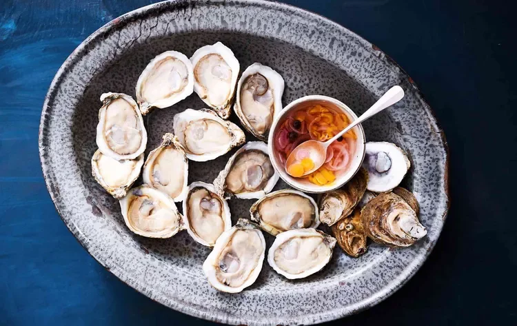 Overhead view of fresh oysters on a speckled serving platter with a bowl of mignonette sauce and lemon wedges