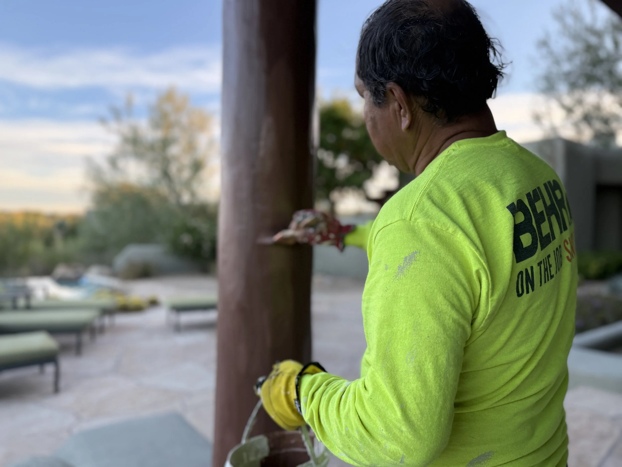 Father staining exterior wood pillars at a Desert Mountain home in Scottsdale AZ during professional exterior house painting project