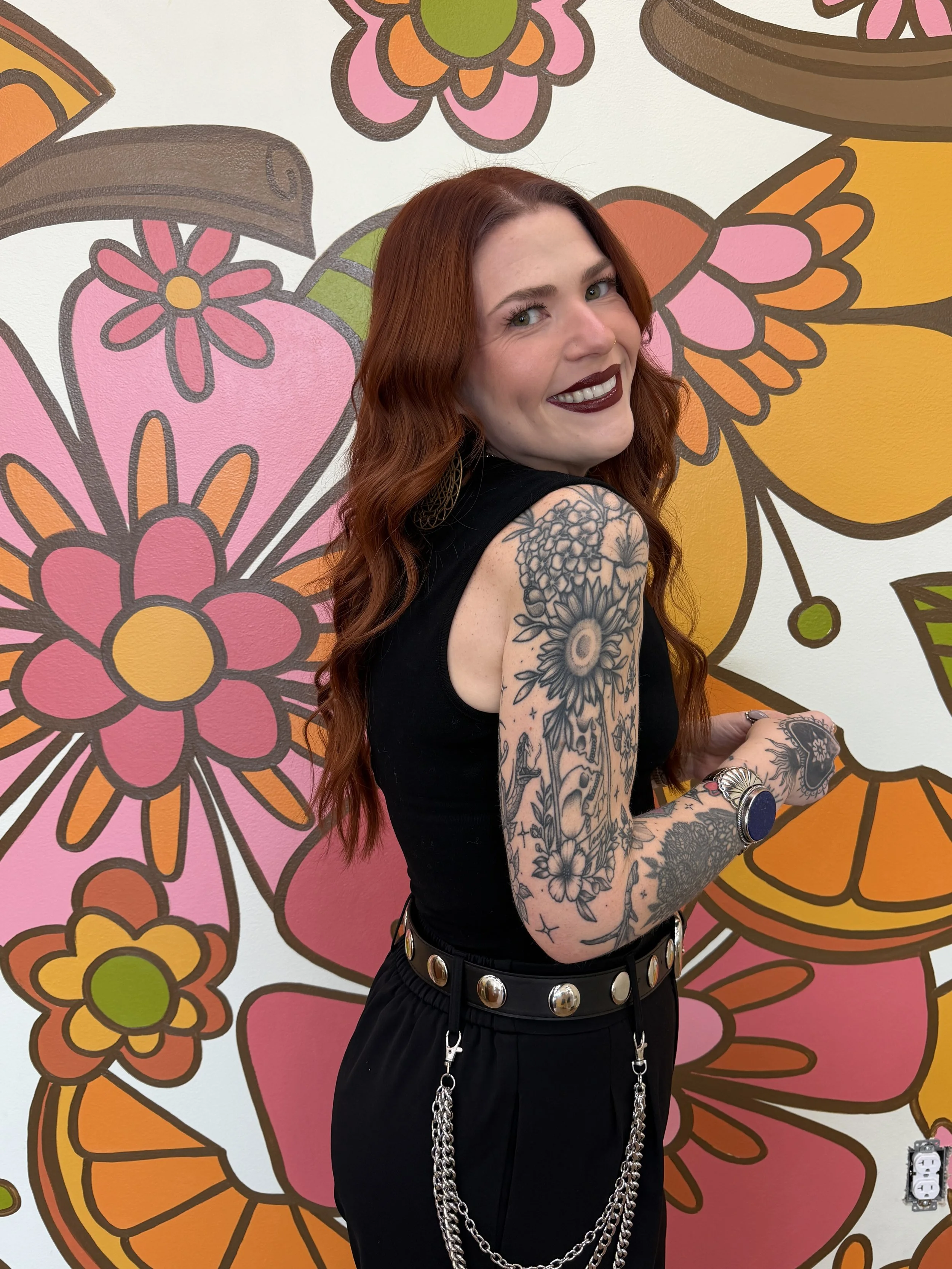 Kaiti smiles over her shoulder in front of the floral mural in Citrus & Cinnamon Salon