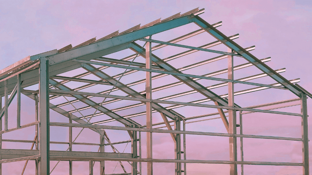 Steel frame of a greenhouse under construction against a pink and purple sky.