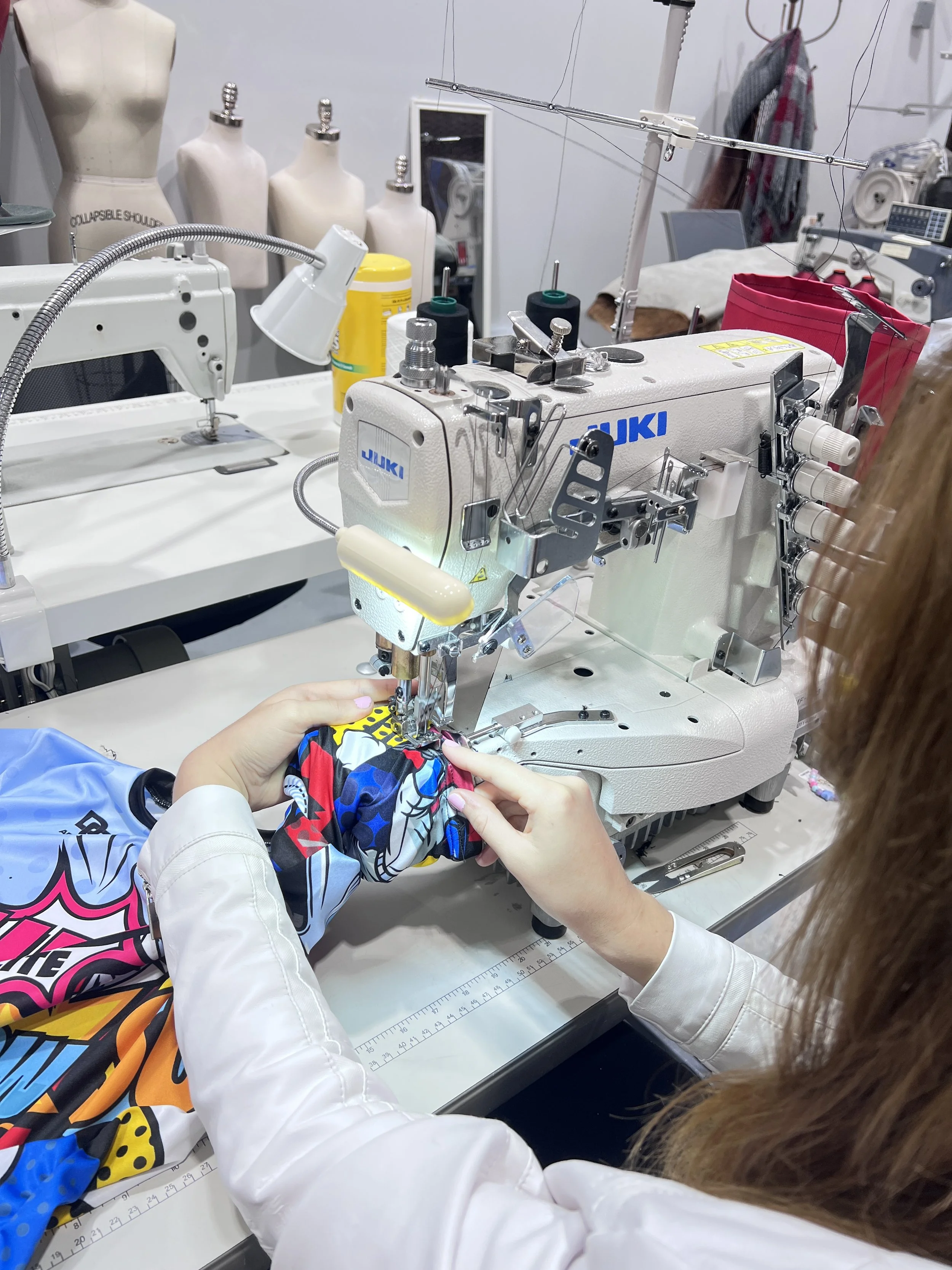 People working on a sewing machine, with mannequin torsos and sewing supplies in the background.