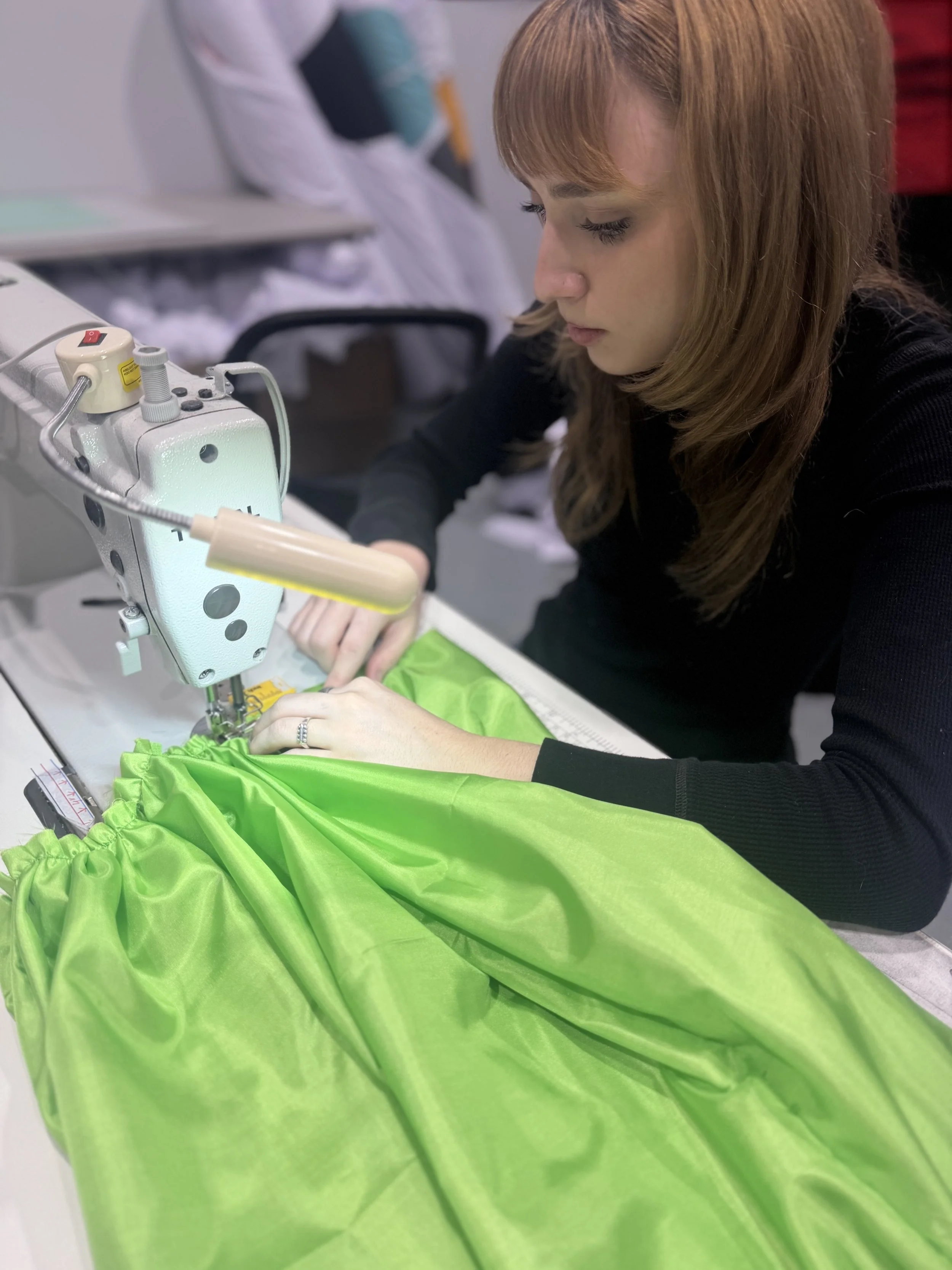 A woman sewing bright green fabric on a sewing machine in a workshop.
