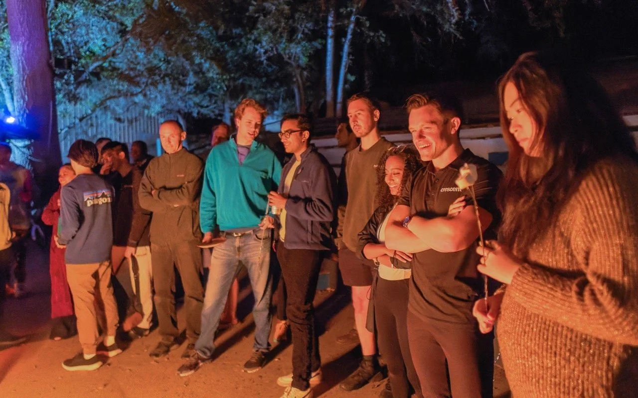 Corporate team members gathered around bonfire in beautiful outdoor setting