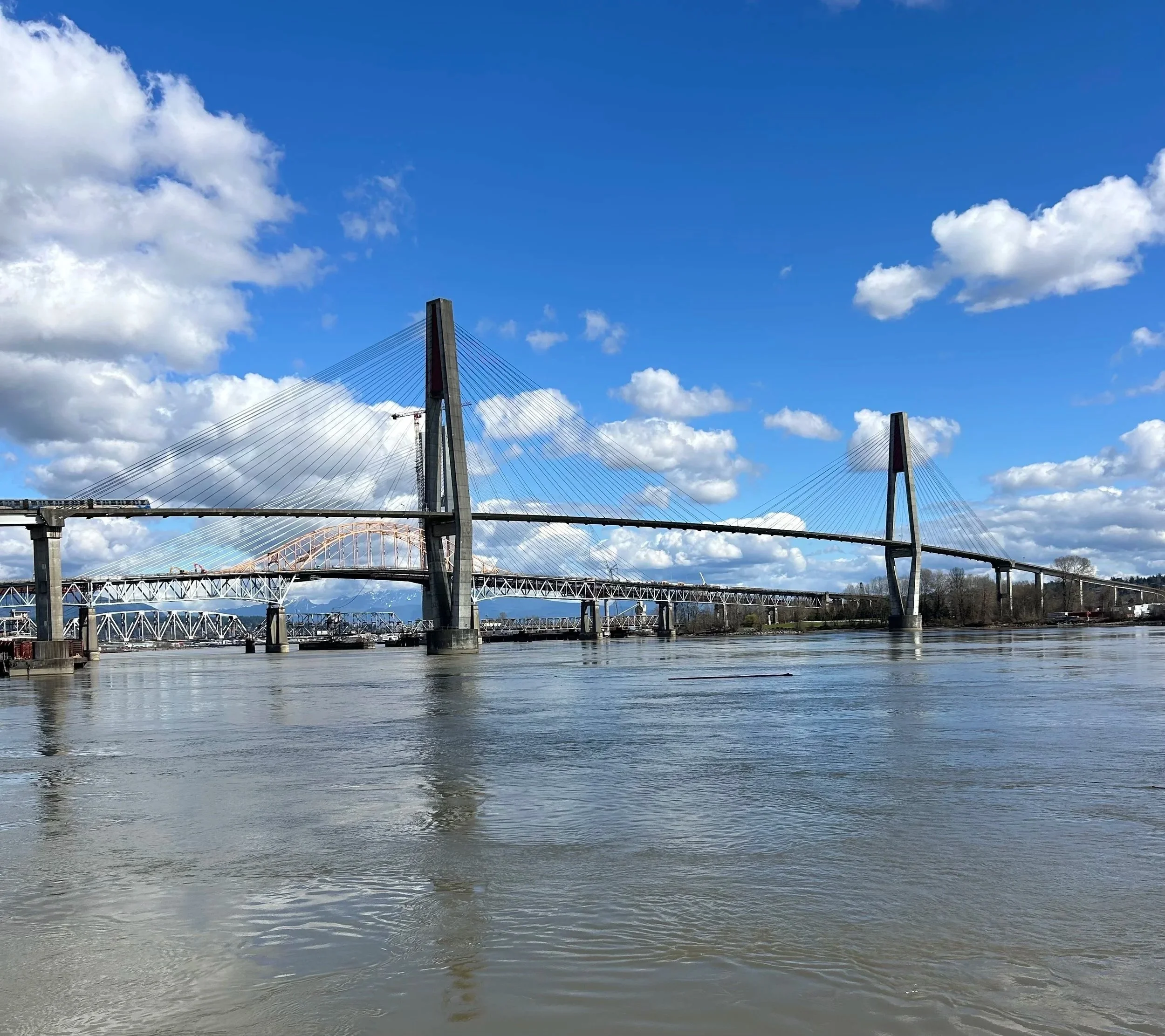 A cityscape view of a bridge over a river with a blue sky and scattered clouds in the background.
