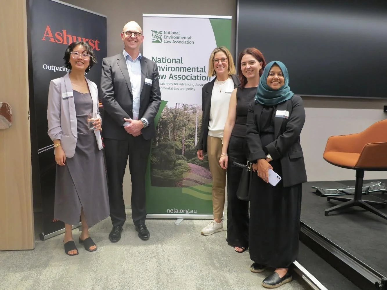 Group of five diverse people at a conference, standing in front of banners for the Australian National Environmental Law Association and Ashurst, smiling for the photo.