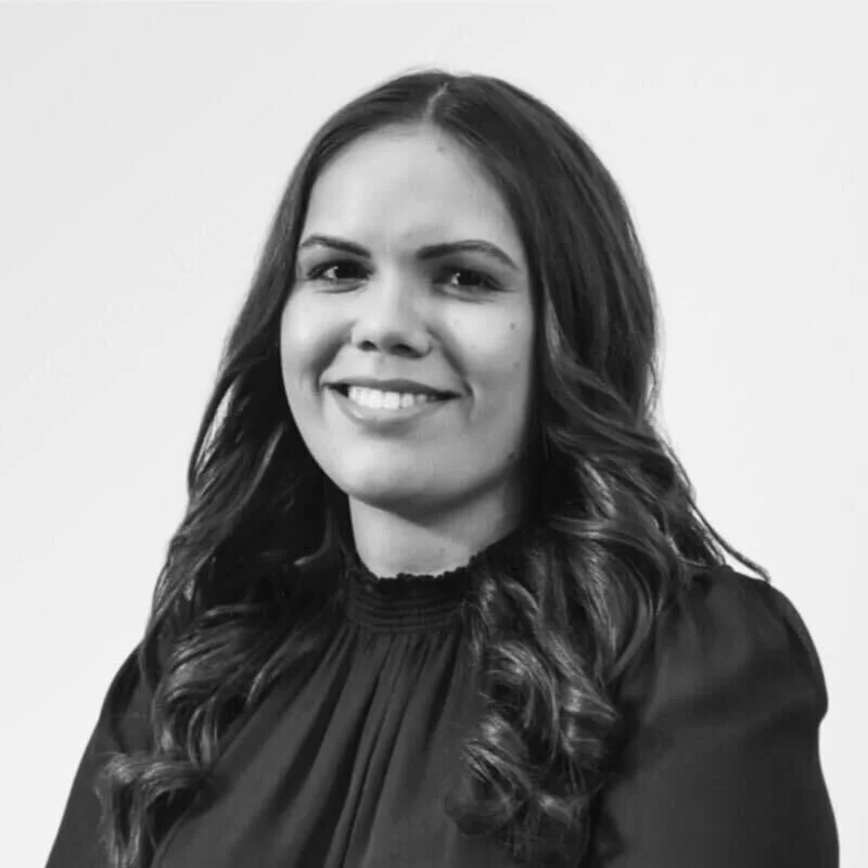 A black and white portrait of a woman with long wavy hair, smiling slightly, wearing a high neckline blouse.