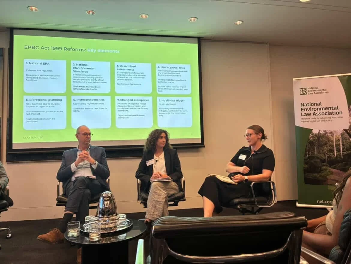 Panel discussion at the National Environmental Law Association event with three speakers seated on stage, two women and one man, with a presentation slide and a banner in the background.