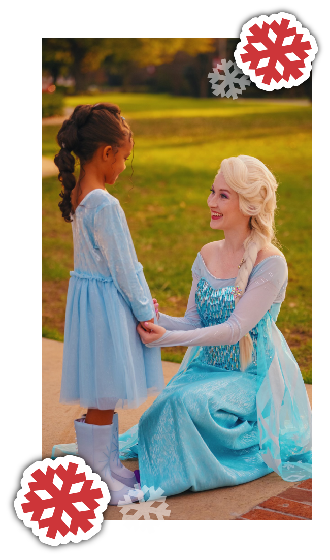A woman dressed as Elsa from Frozen kneeling and holding hands with a young girl in a blue dress and white boots outdoors during fall, with snowflake stickers added to the image.