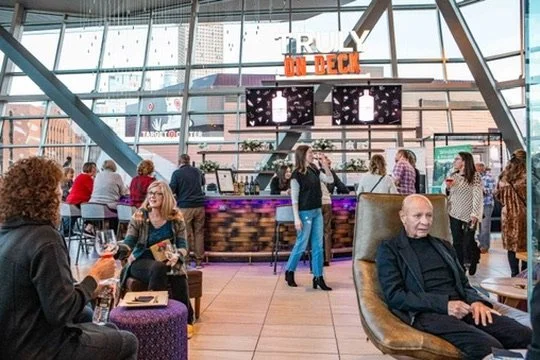 People socializing in an airport lounge with a bar and digital display screens behind the bar.