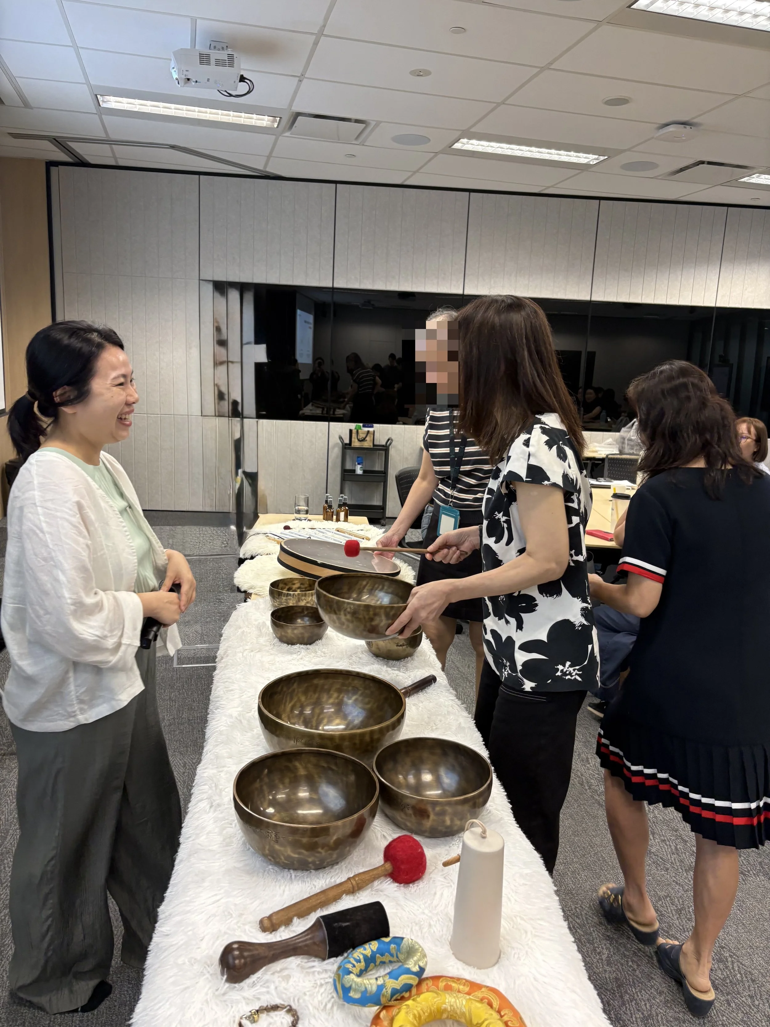 Group of people participating in a sound healing or meditation session indoors, with singing bowls, candles, and decorative items on a wooden floor.