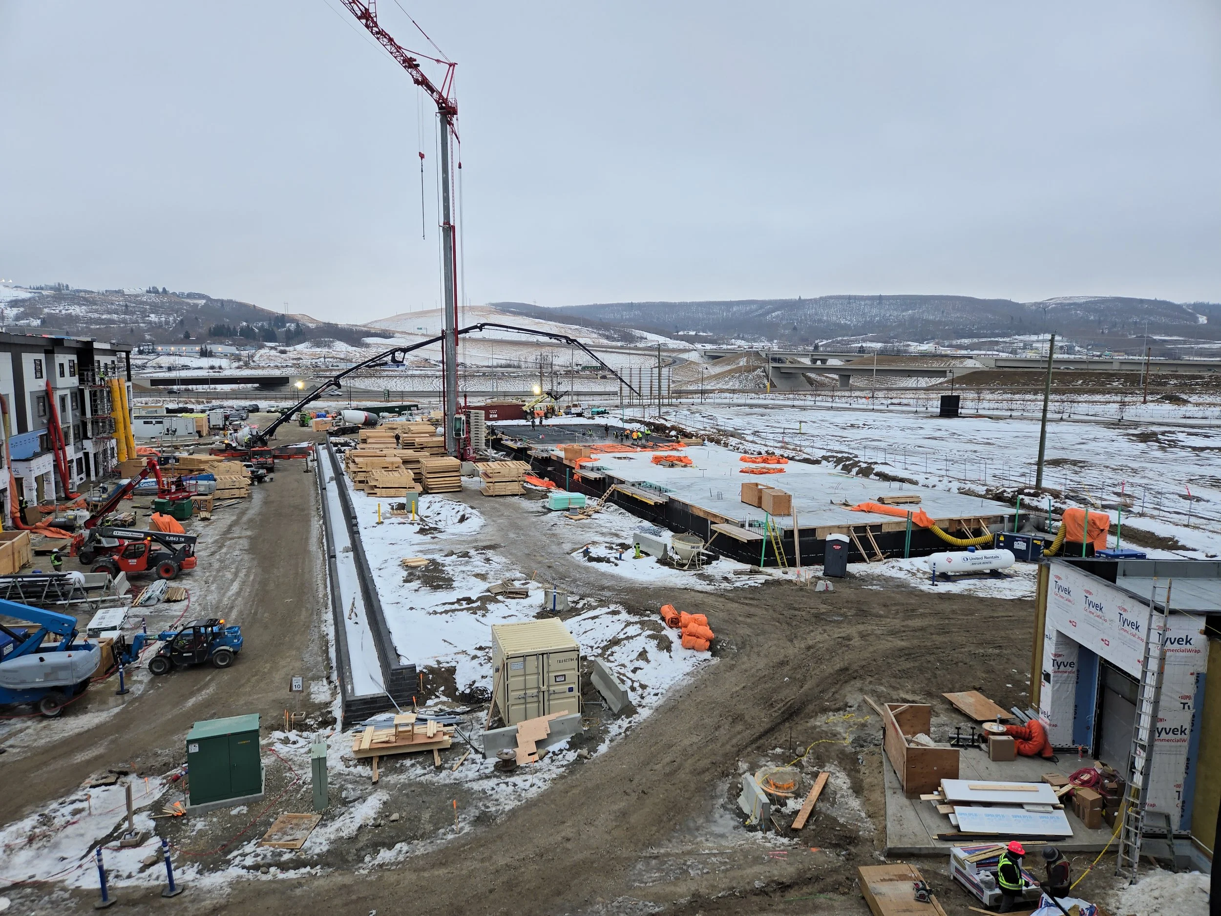 Wide aerial view of a large‑scale construction site featuring active building zones, cranes, staging areas, and winter conditions