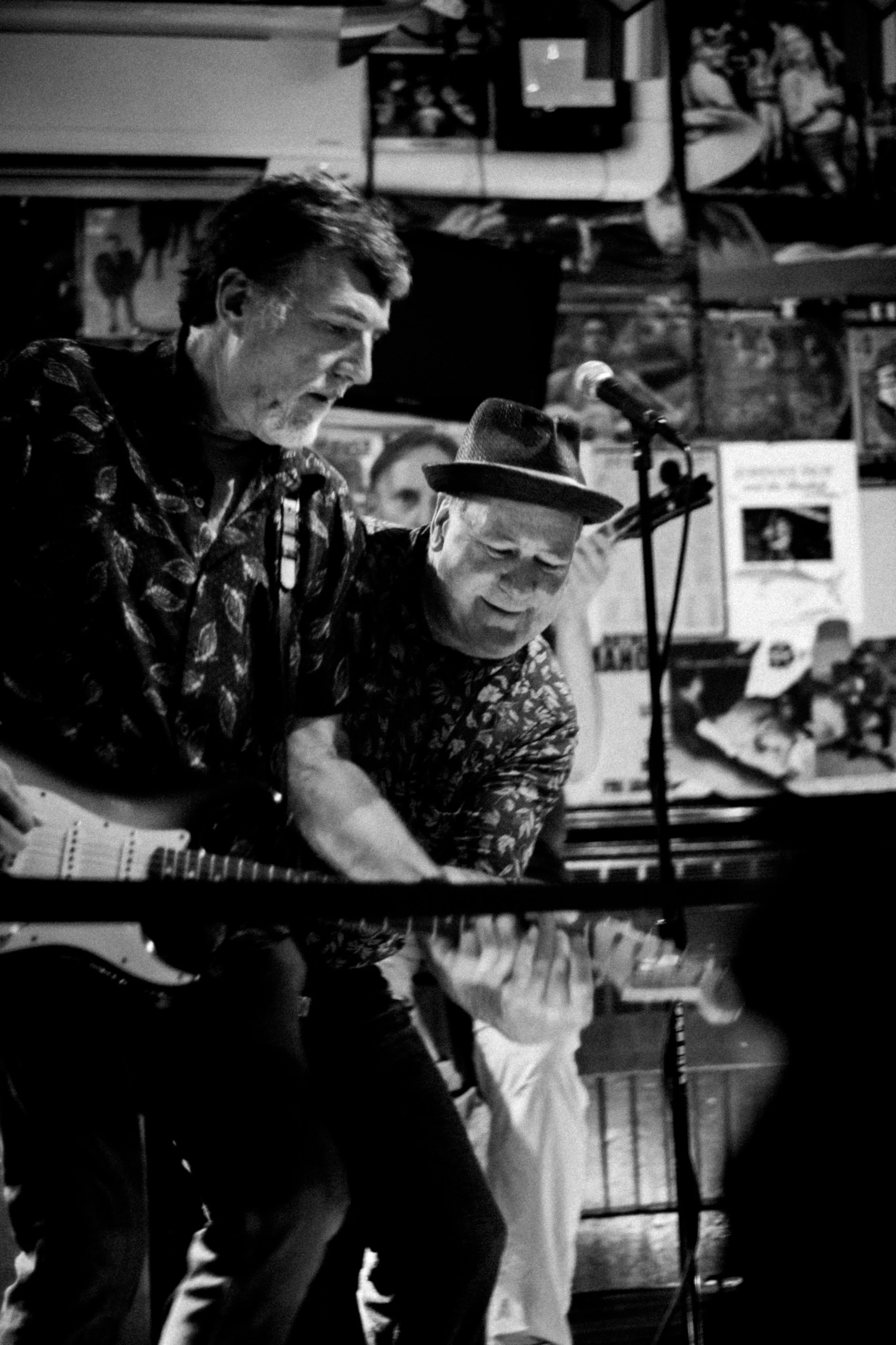 Two men performing music together in a venue, with one playing guitar and both singing into a microphone.