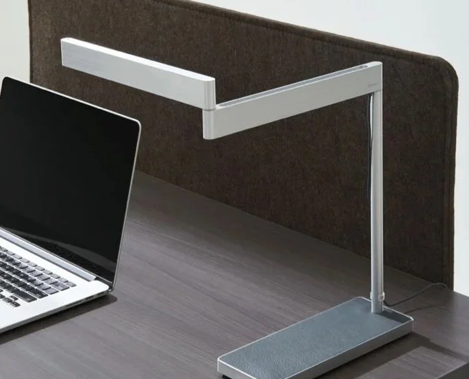 A desk with a laptop and a modern adjustable desk lamp.