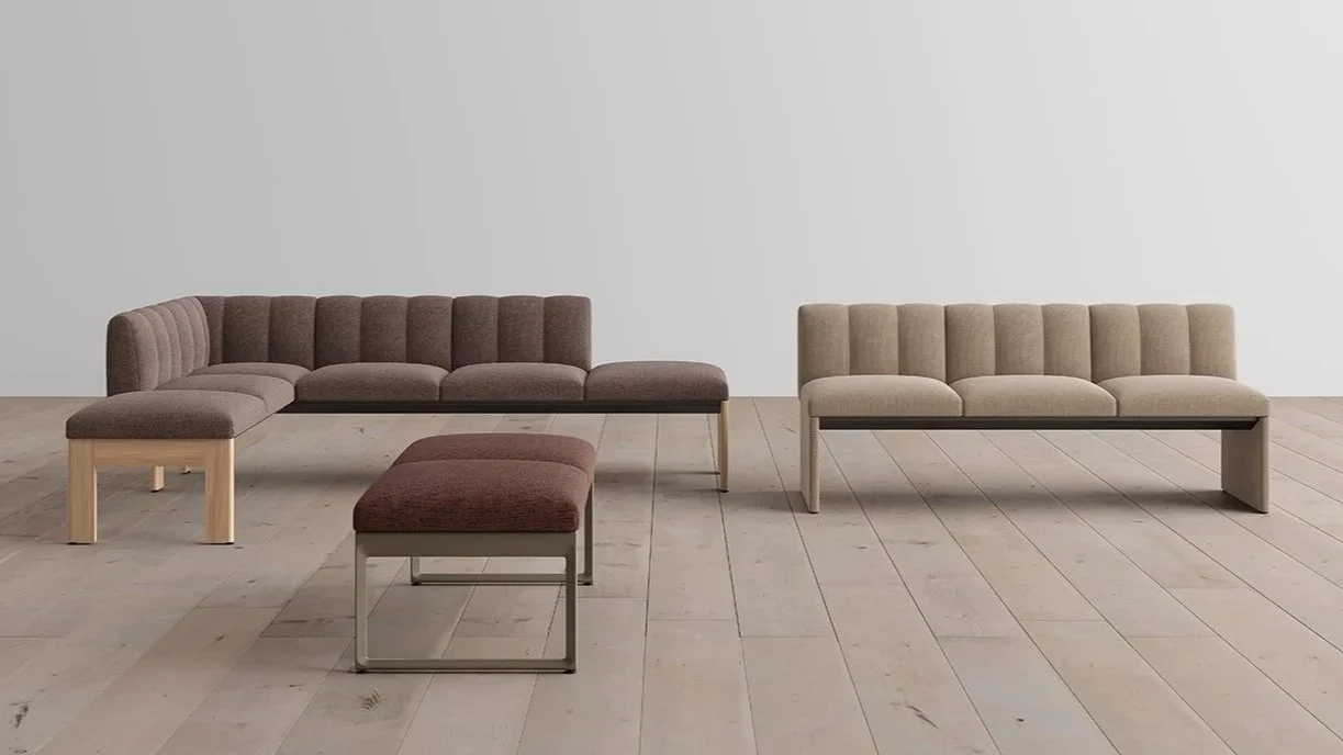 Living room with two modern upholstered sofas, one beige and one brown, and a matching ottoman, all placed on light wood flooring against a plain white wall.