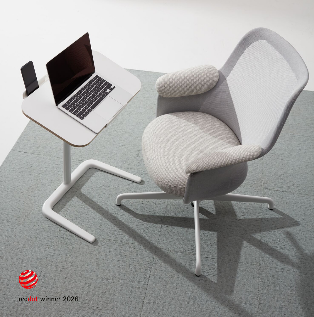 A modern workspace with a light-colored ergonomic chair, a small white table holding a silver laptop and a smartphone, all on a light gray carpet.