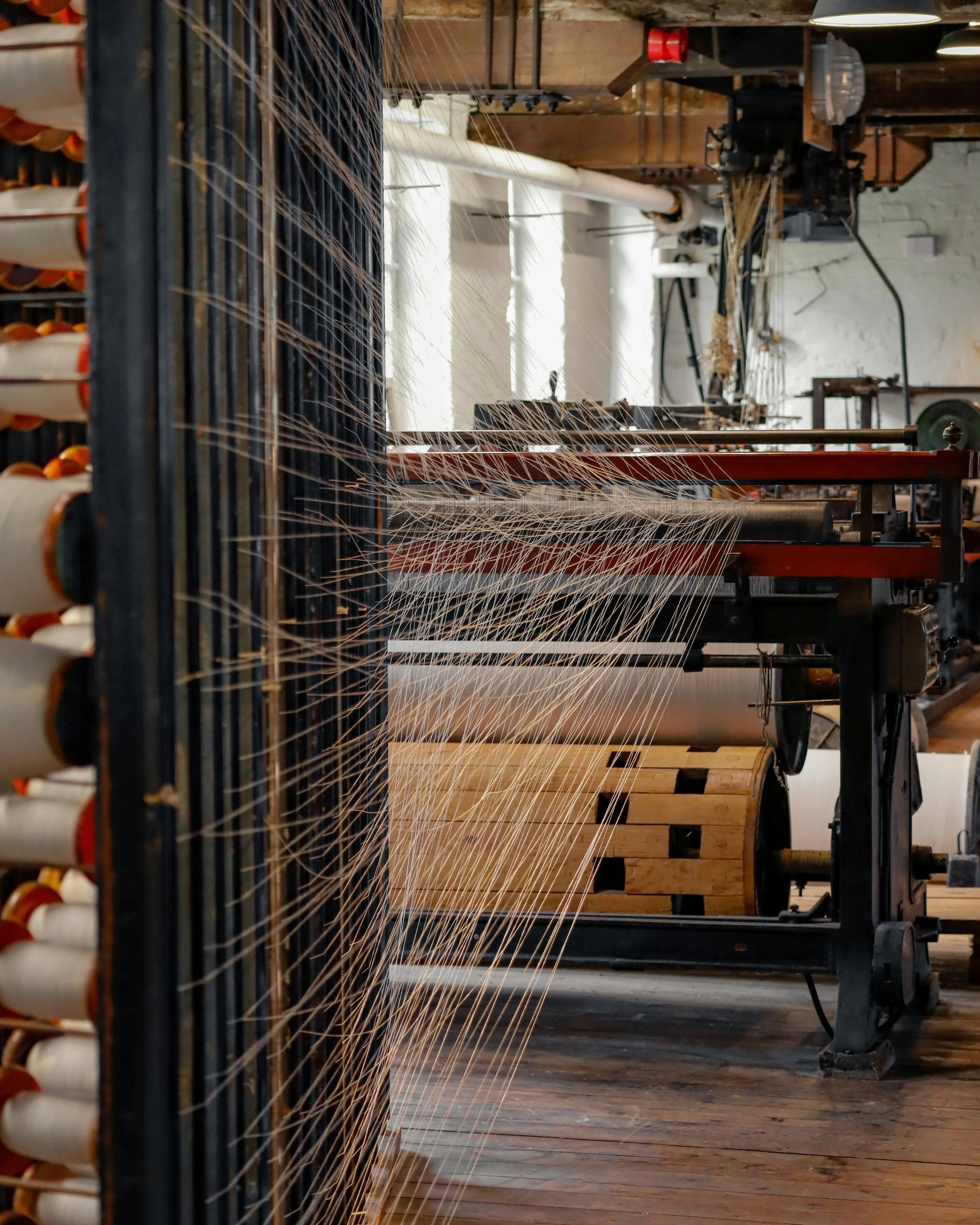 Industrial textile weaving machine with spools of thread, weaving multiple strands on a wooden floor in a factory setting.