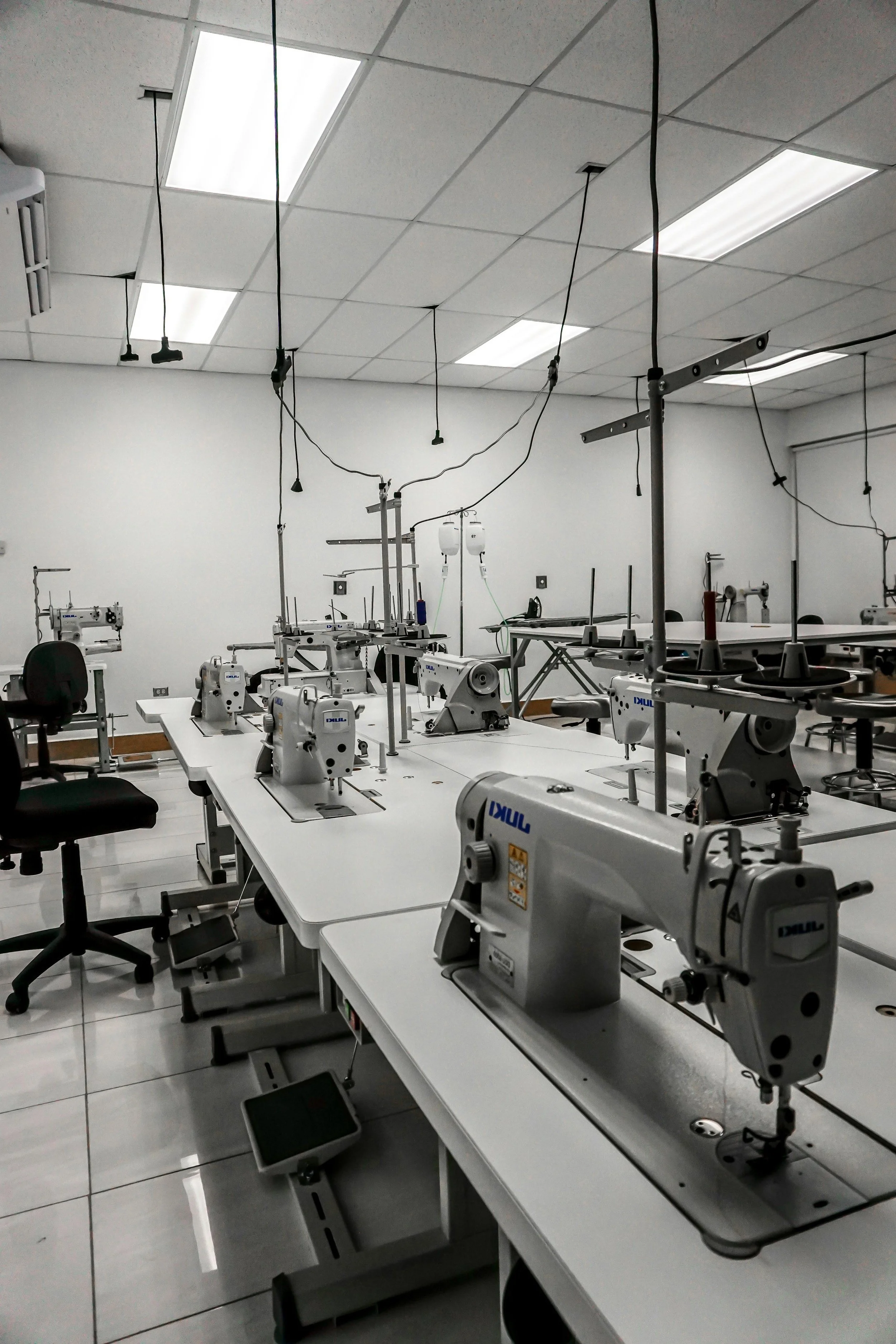 Sewing machines in a factory setting with overhead lights and scattered chairs at Authent office.