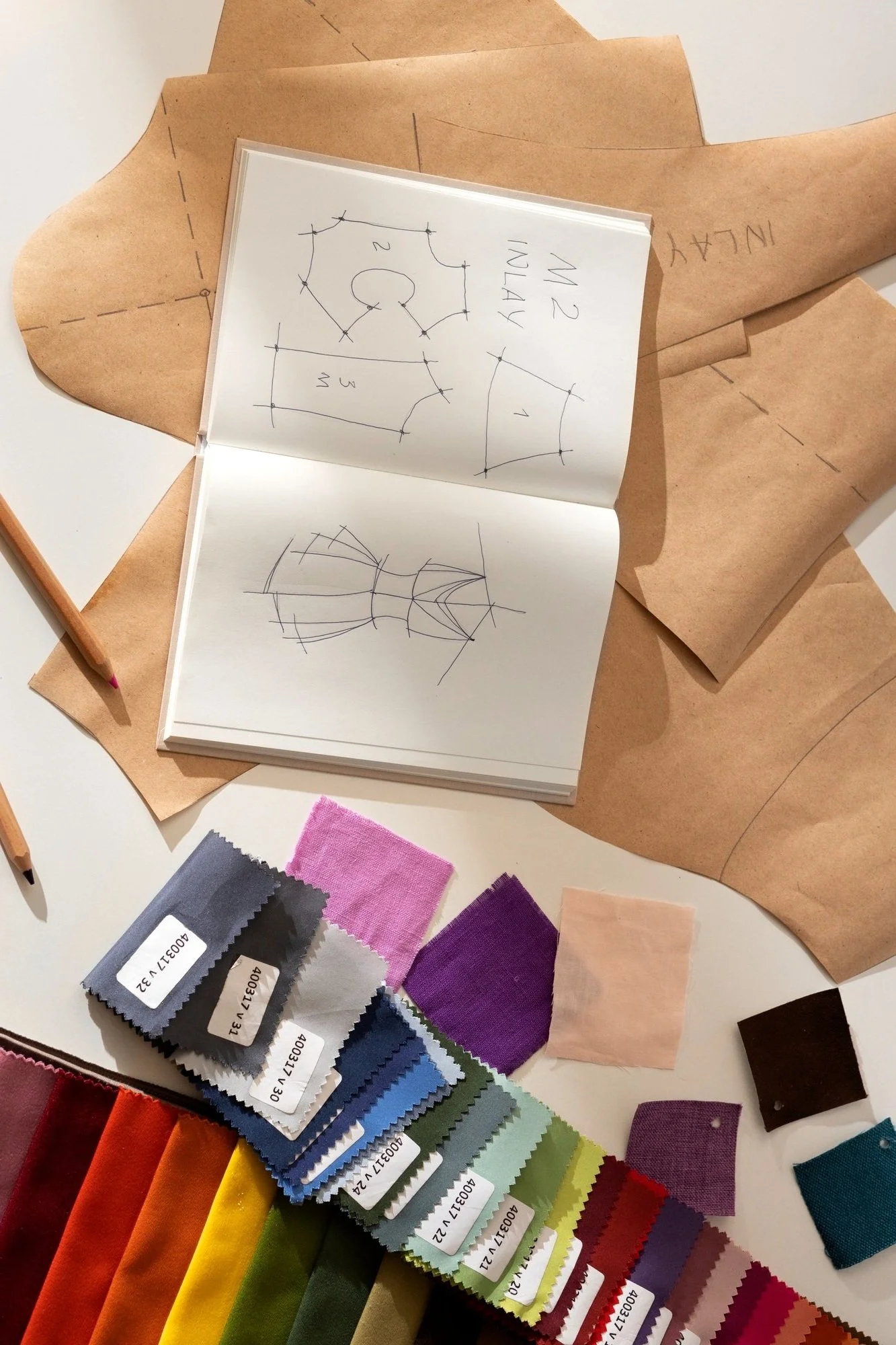 Sewing pattern sketches on paper with fabric samples and swatch book on a table at Authent Office.