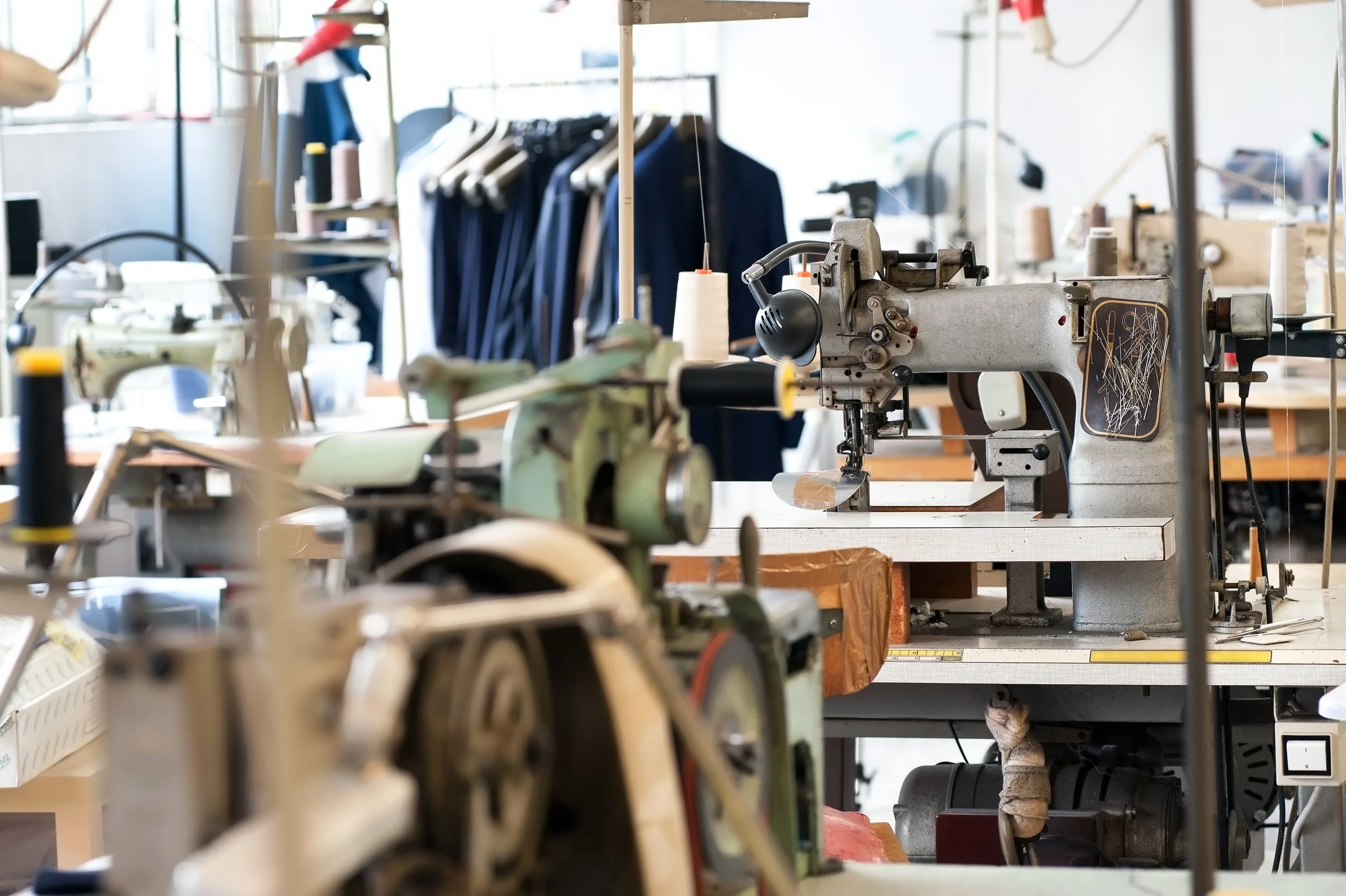 Industrial sewing machines in a garment factory with clothing racks in the background art Authent office.