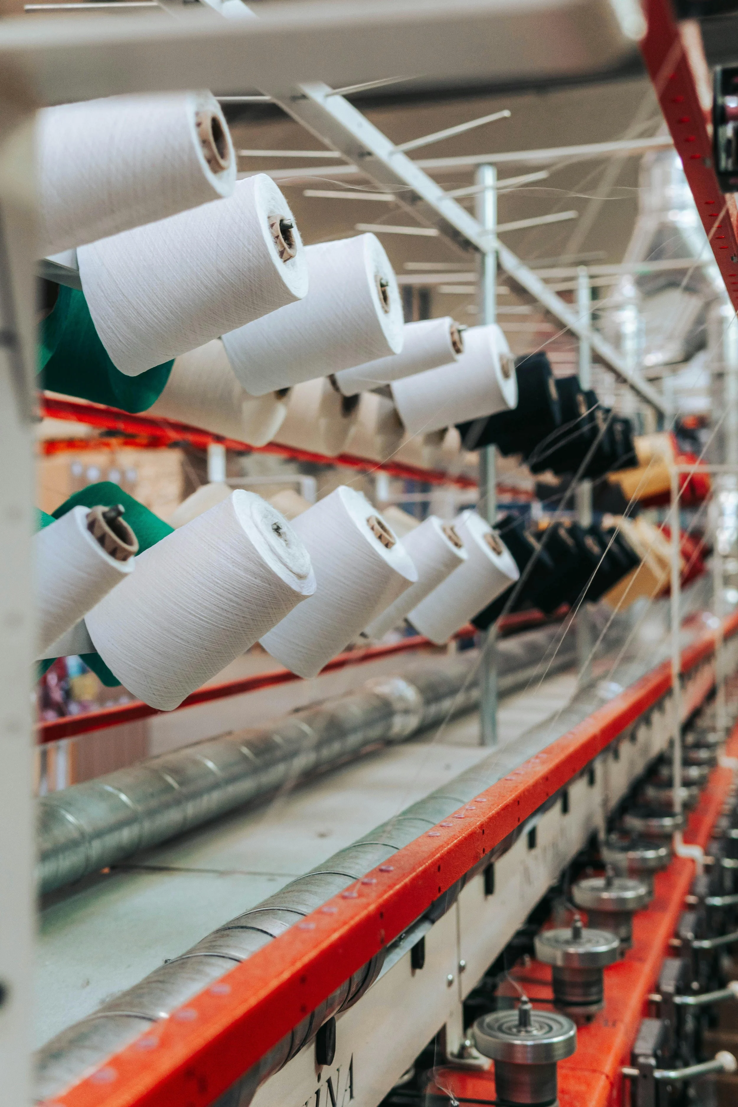 Textile factory with spools of colored thread, including white and black, on a rack above weaving machinery.