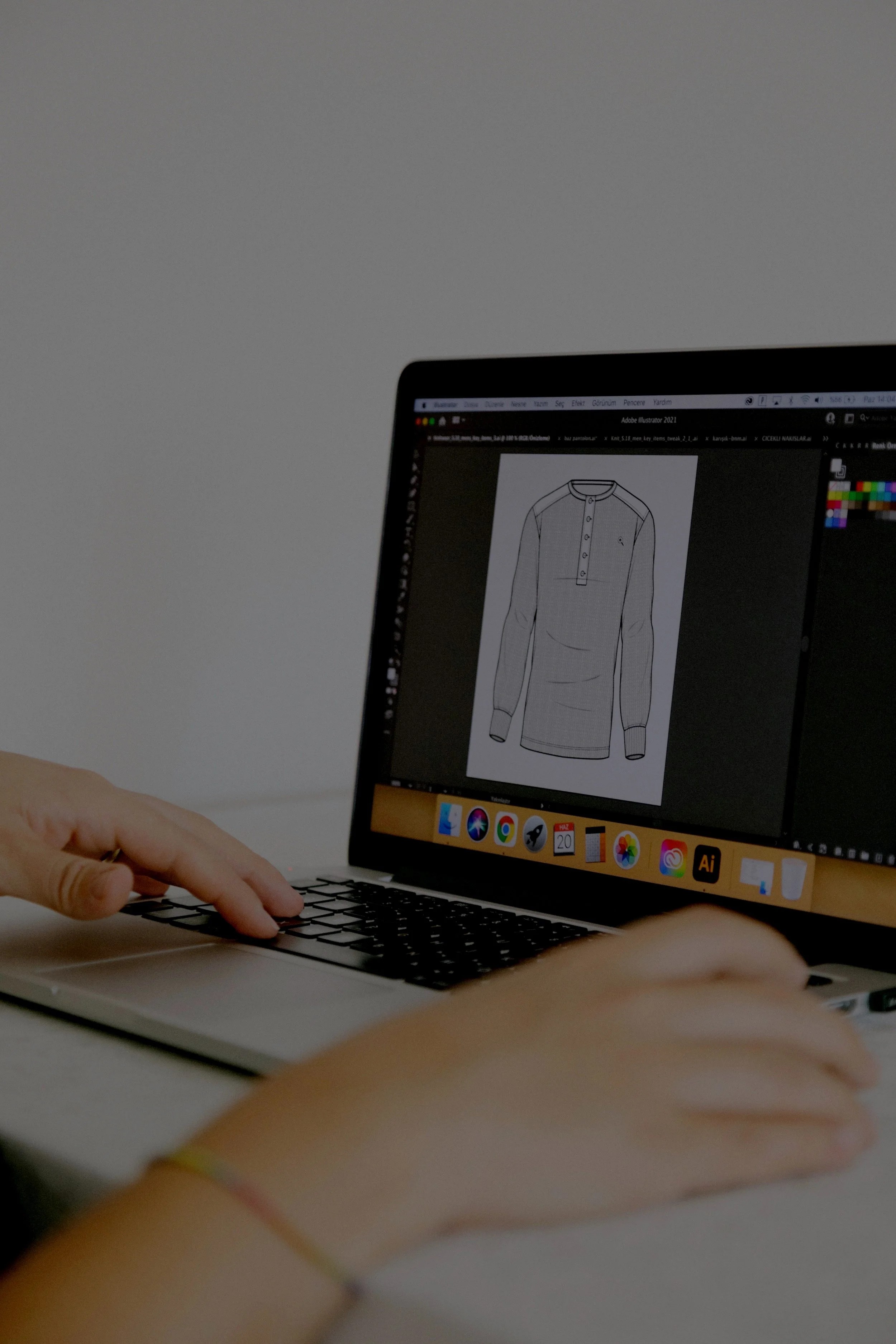 Person using a laptop with graphic design software displaying a shirt illustration on the screen. Designing apparel on adobe software to show mockup for understanding of the product.