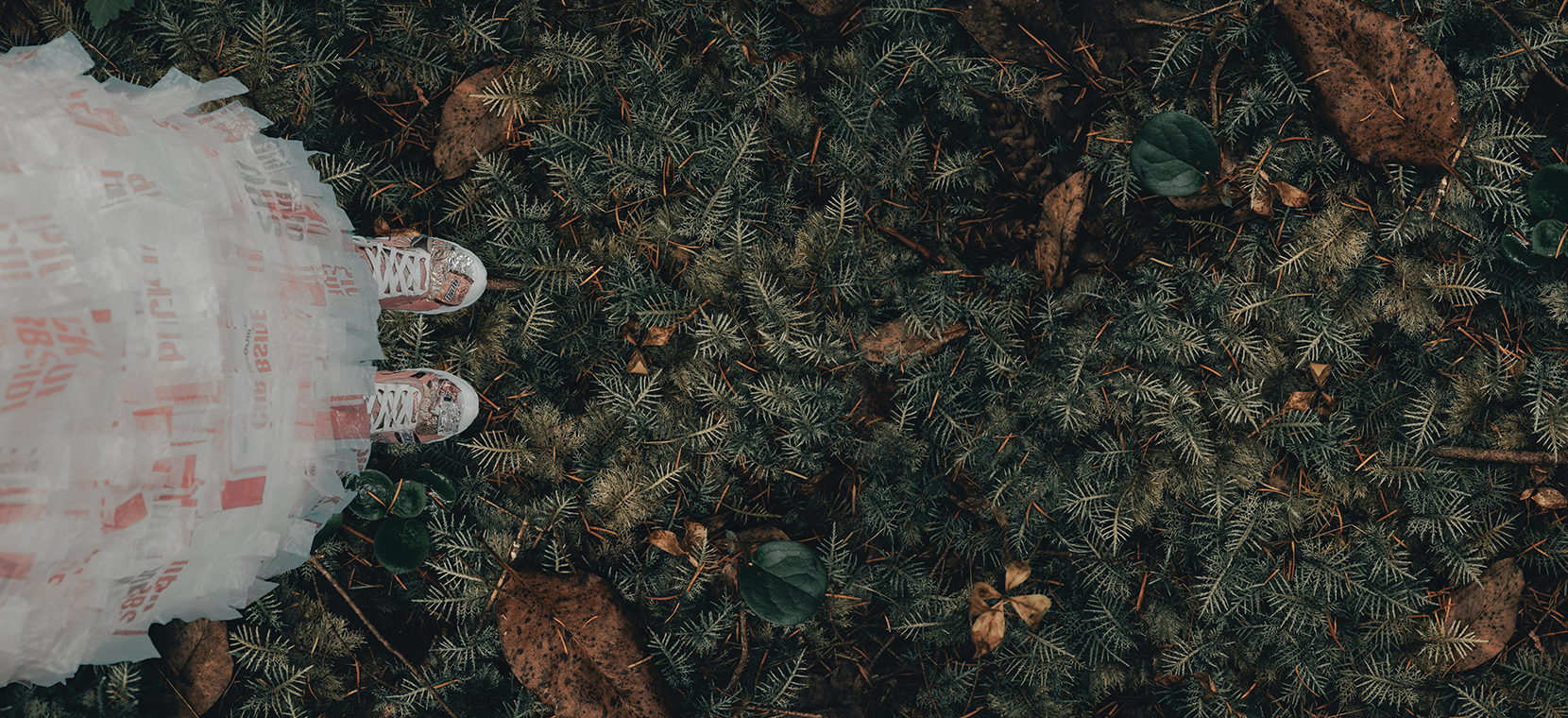 Overhead view of a person wearing sneakers and a plastic skirt standing on a forest floor with green foliage and fallen leaves. Sustainable initiatives at Authent.