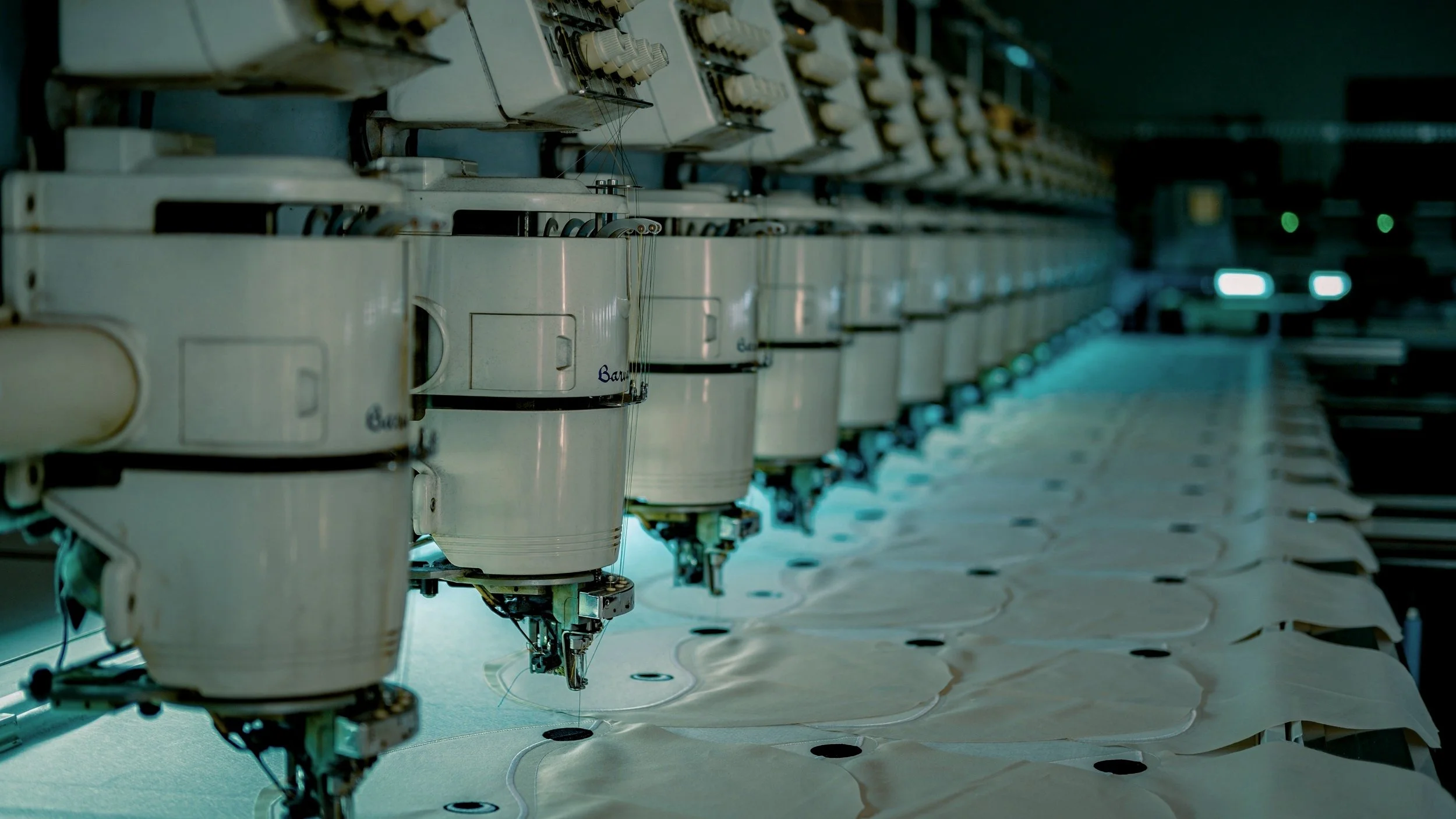Row of industrial embroidery machines stitching fabric in a factory.