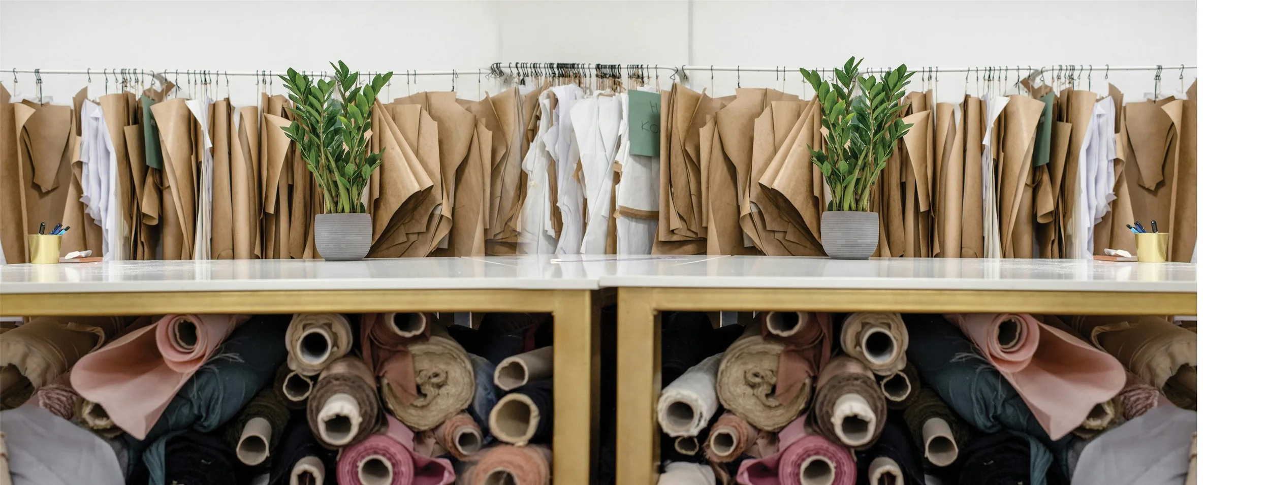 Fabric rolls and sewing patterns in a fashion studio workspace with potted plants on a table at Authent Office.