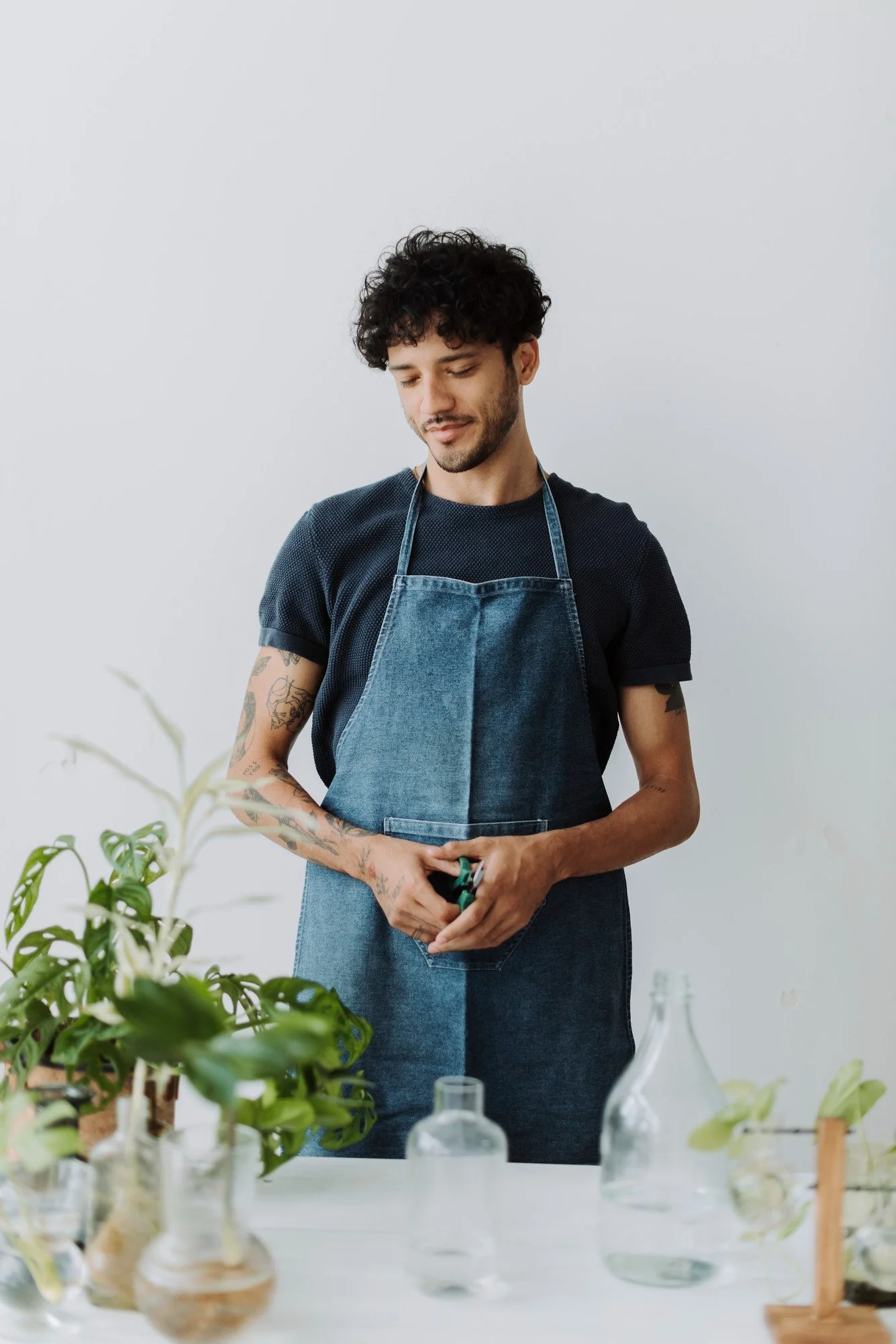 Man wearing blue apron with logo printed standing by a table with plants and glass bottles. - garment manufactured at Authent.