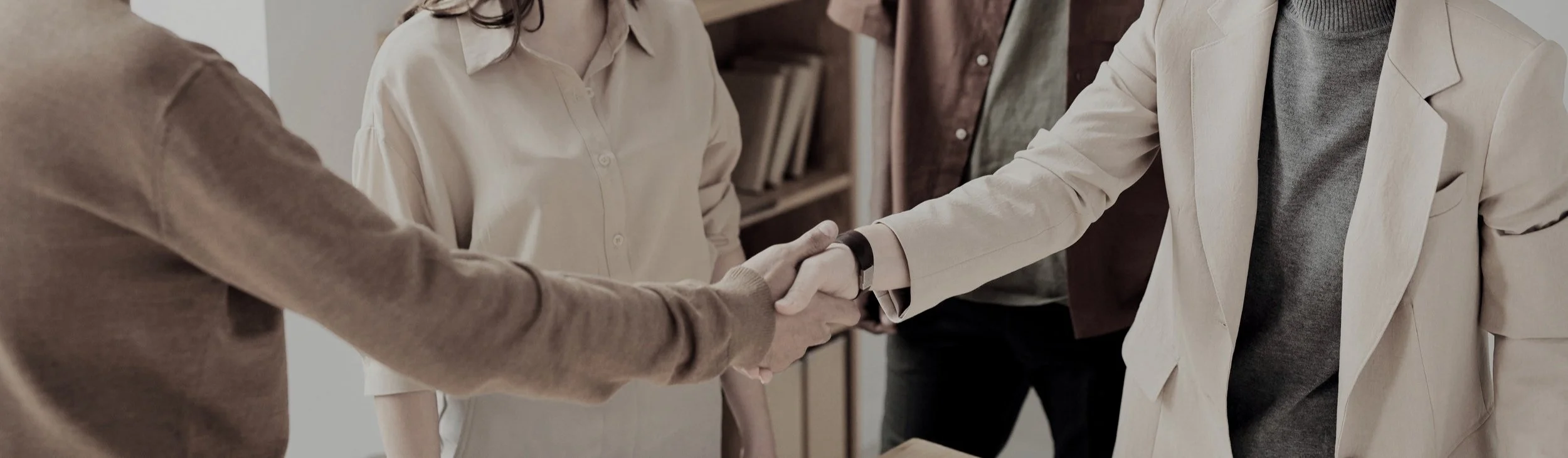 Two people shaking hands in an office setting with two others in the background. Happy clients at Authent.