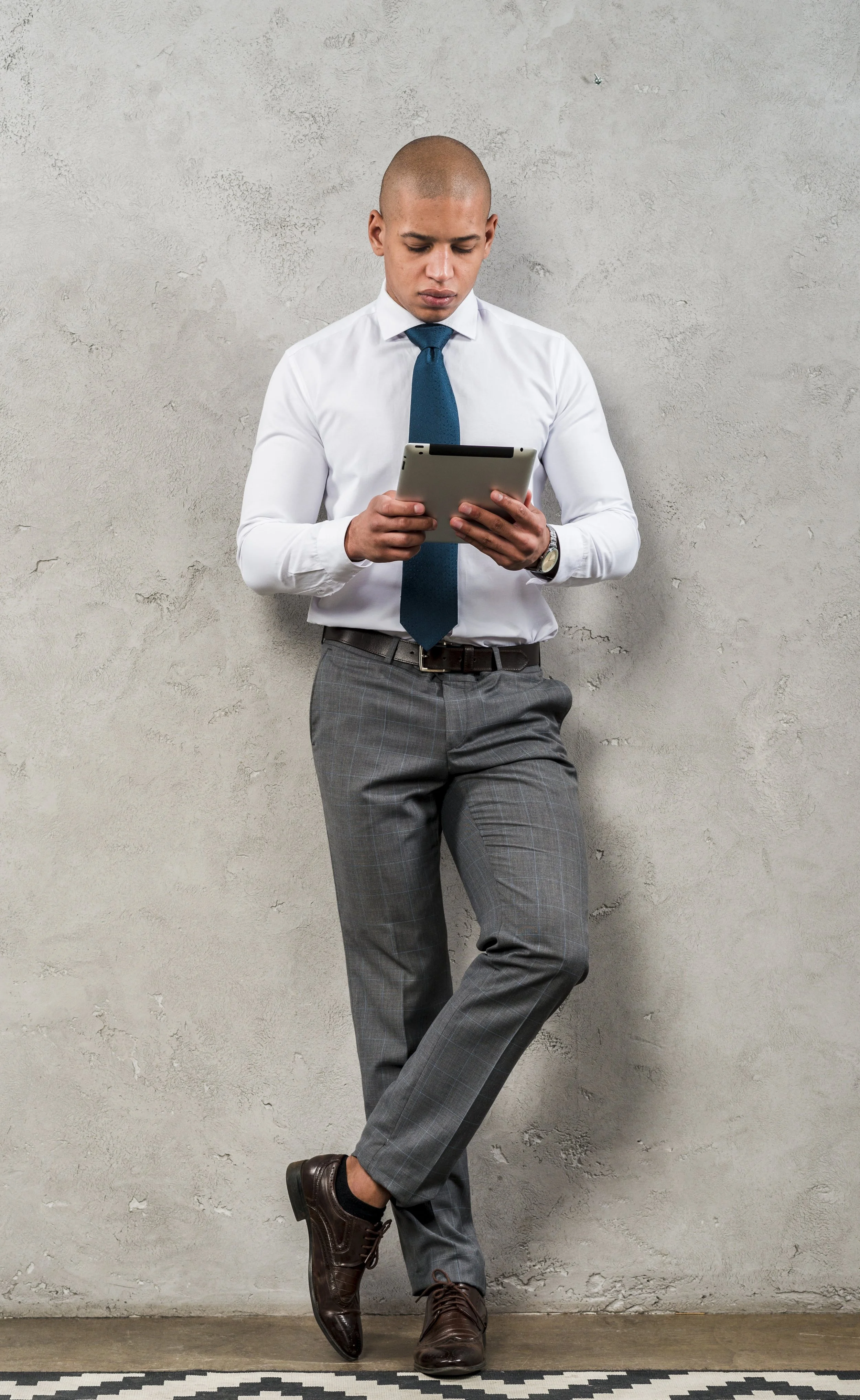 Man in high quality formal white shirt with logo embroidered using tablet against gray wall - garment manufactured at Authent.