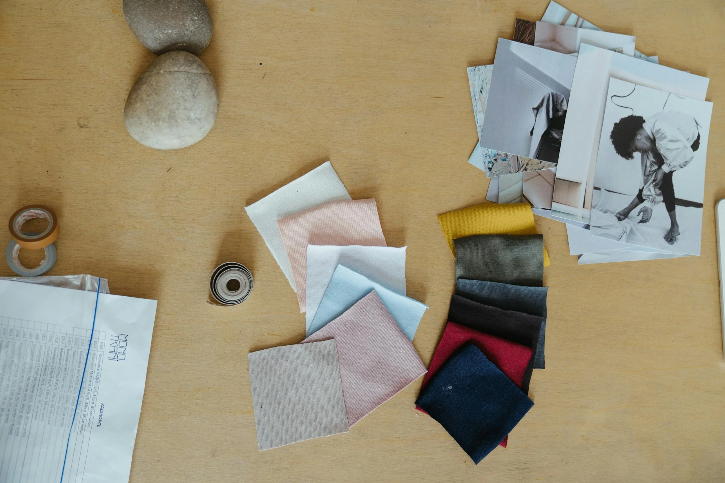 Fabric swatches in various colors, photographs, rocks, tape, and a printed document on a wooden surface at Authent office.