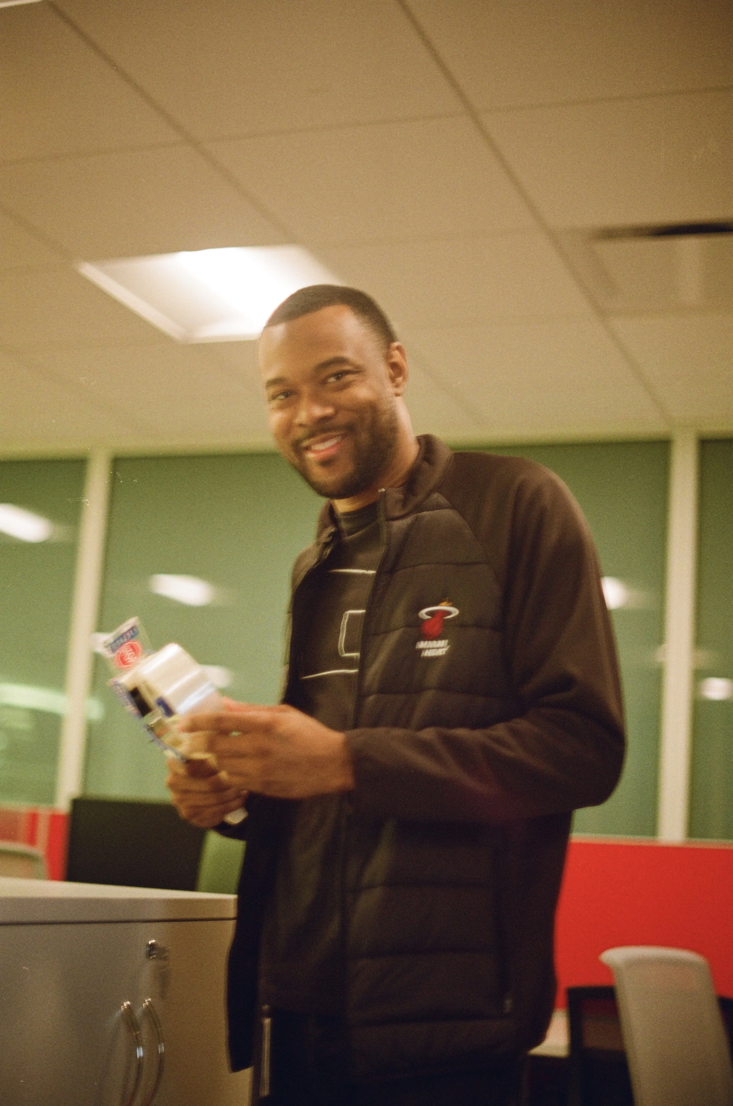 A man smiling and holding snacks in an office break room.