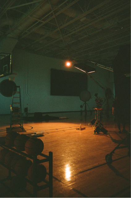 Studio with lighting and camera equipment, empty gym floor, and a large screen or monitor on the wall.